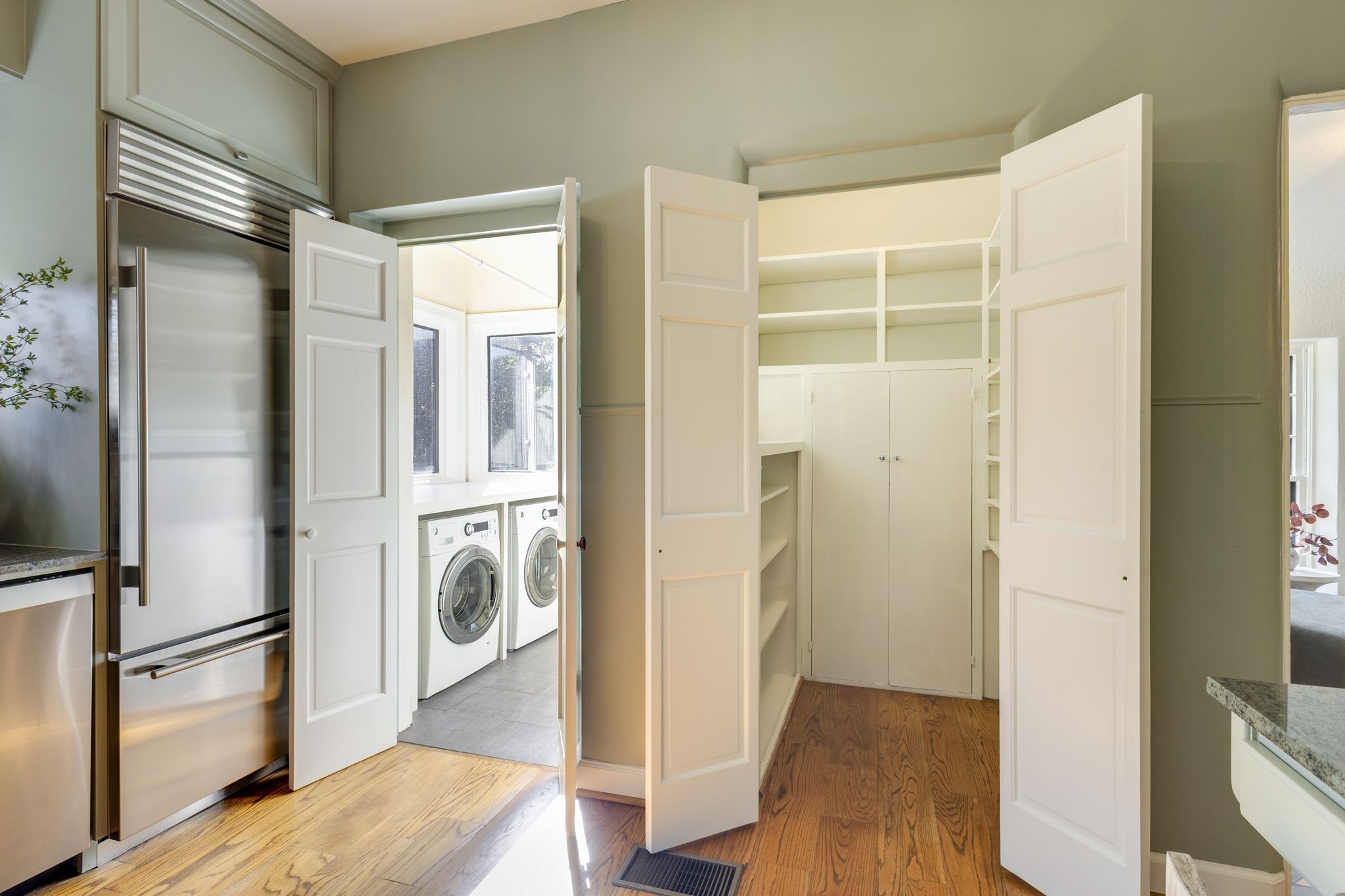 Utility area with built-in storage, front-loading laundry machines, and a stainless-steel refrigerator.