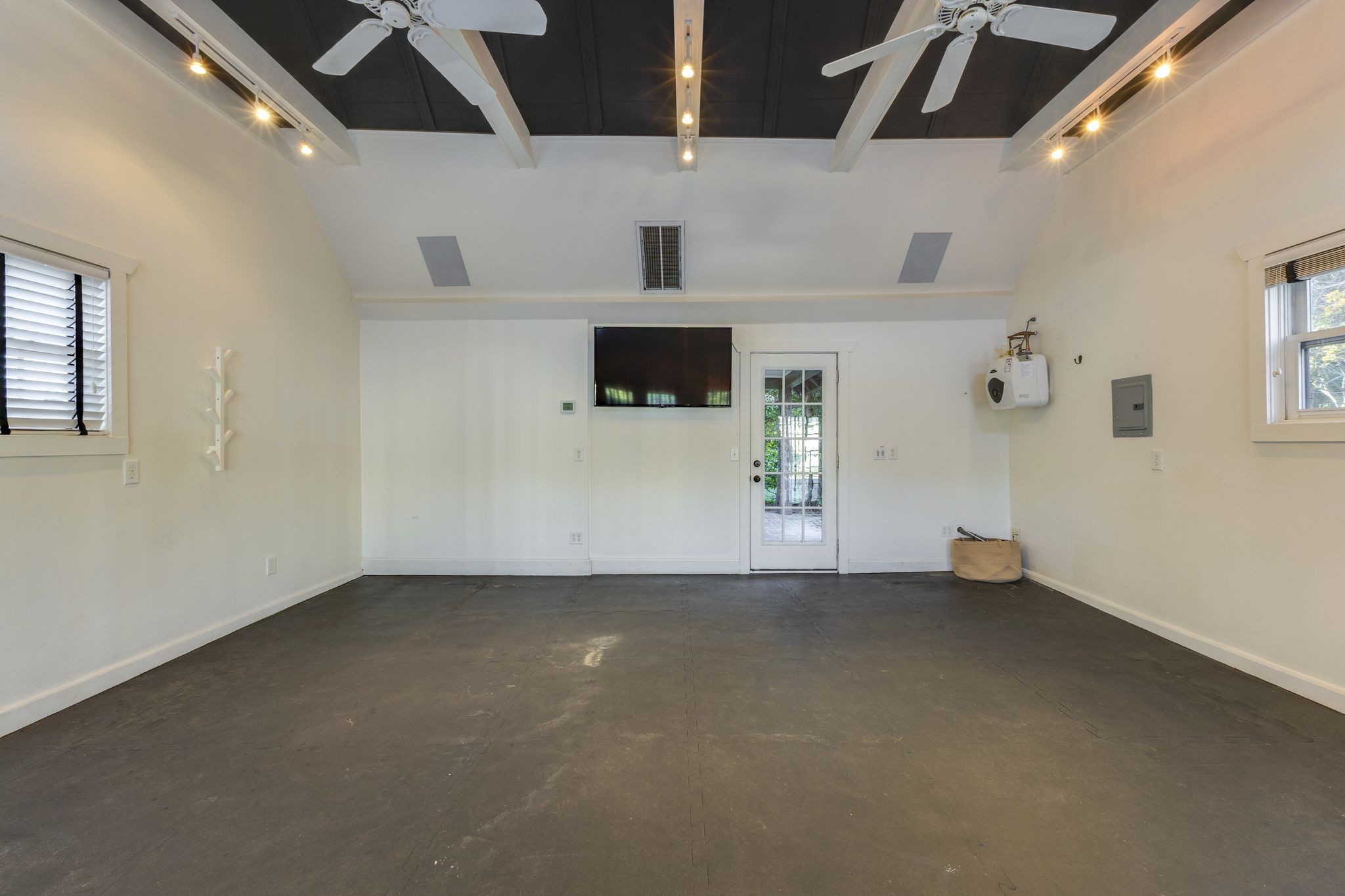 Empty garage with dark floor mats, ceiling fans, and a wall-mounted television.