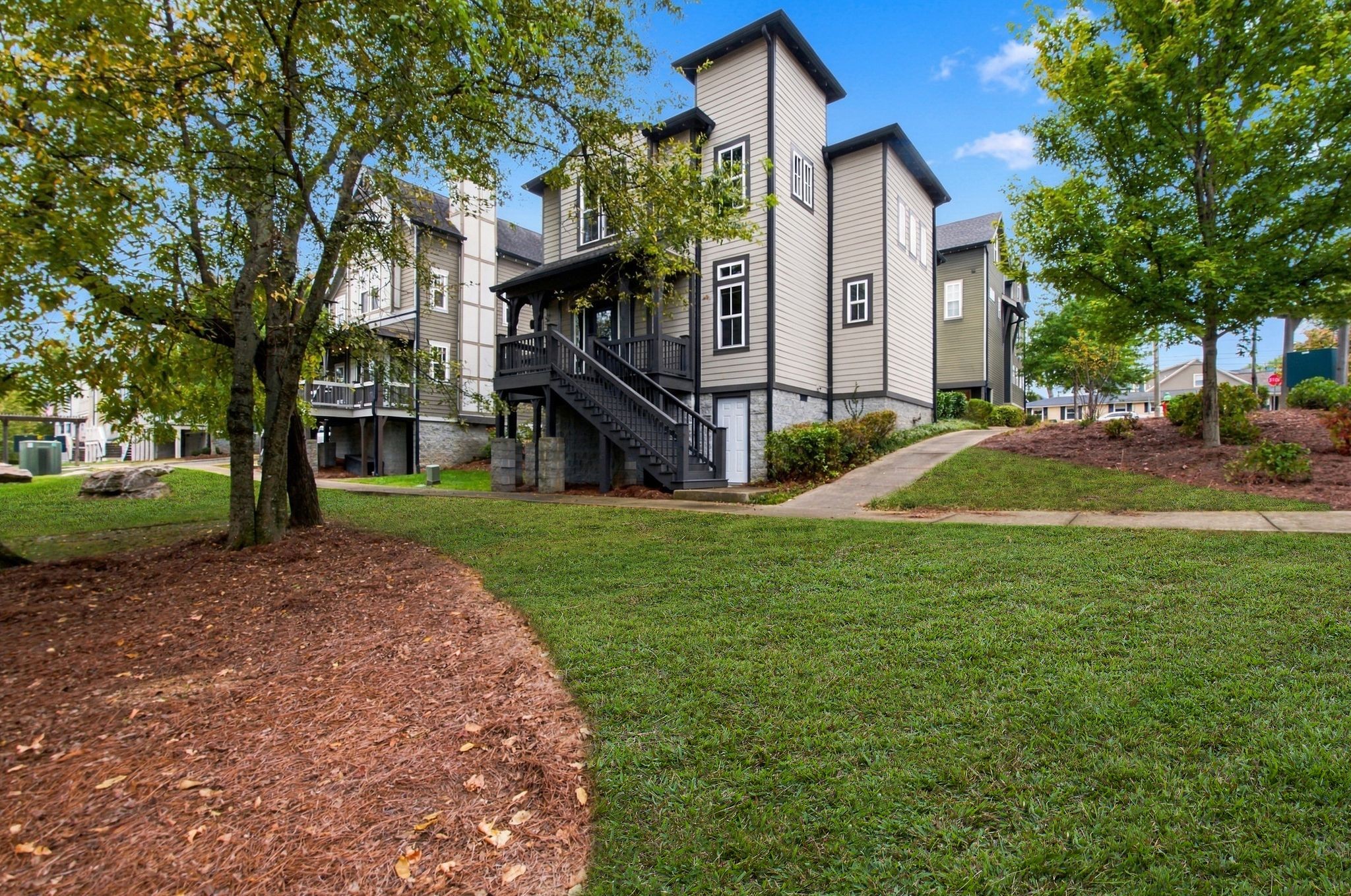Gray multi-story home with a raised black porch, exterior staircase, and stone foundation.