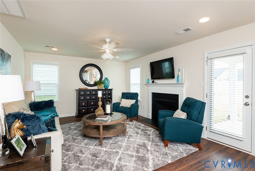Furnished living room with teal armchairs, round coffee table, and fireplace beneath a wall-mounted television.