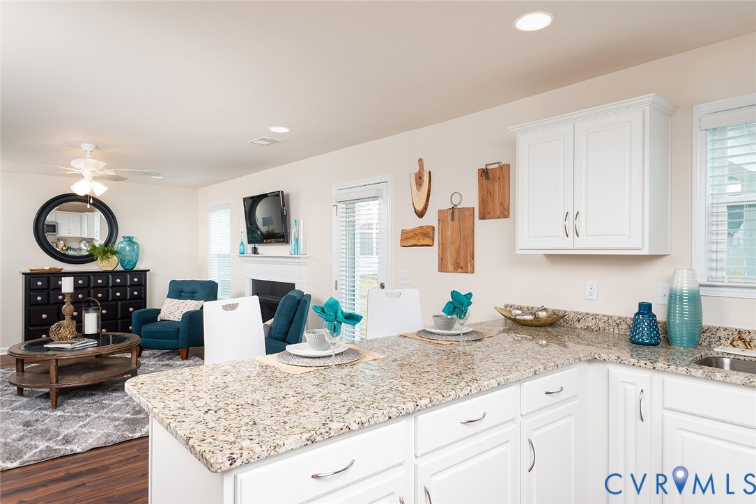 Kitchen with a granite peninsula and white cabinetry opening to a furnished living area.