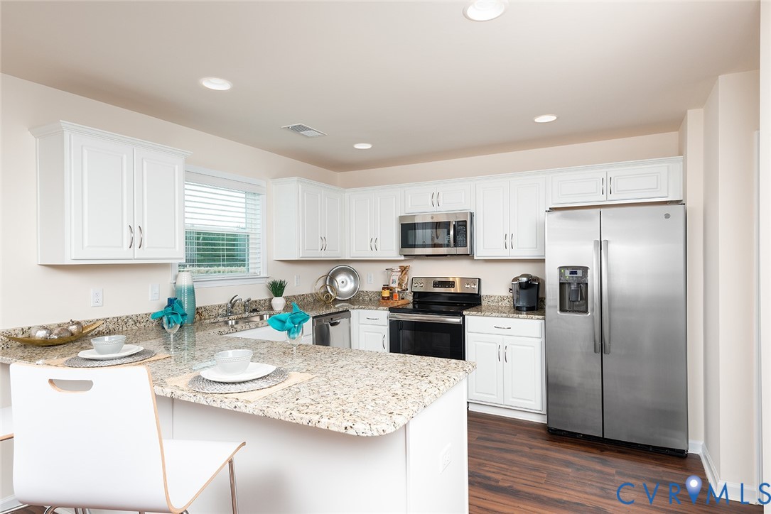Kitchen with a granite island, white cabinetry, and stainless steel appliances.