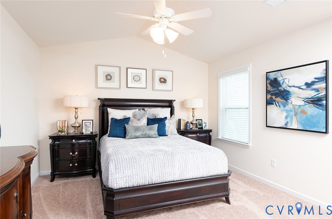 Furnished bedroom with a dark wood bed, blue accent pillows, framed artwork, and a ceiling fan.