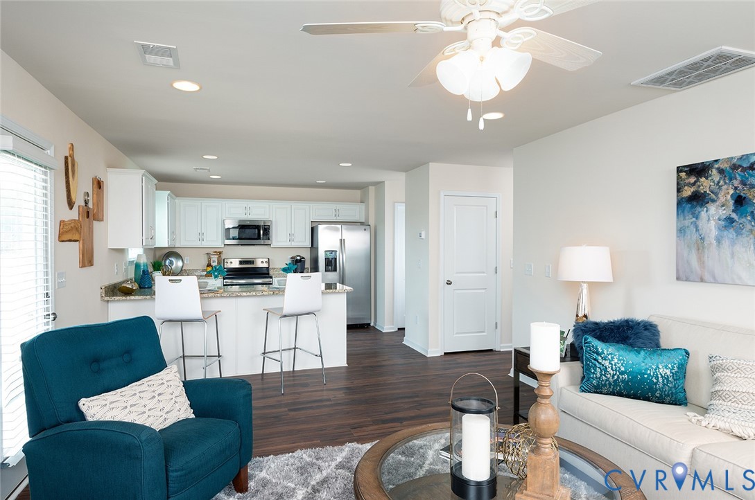 Open-plan living room and kitchen with a teal armchair, breakfast bar, and stainless steel appliances.