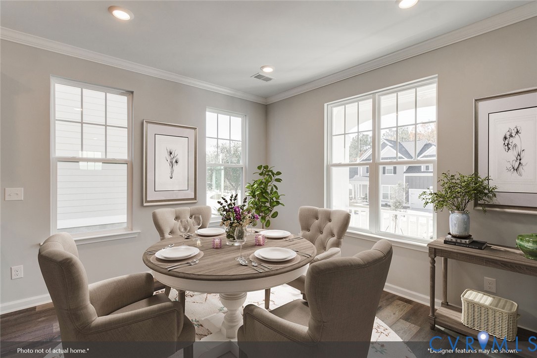 Staged dining room with a round set table, upholstered chairs, botanical prints, and large windows.