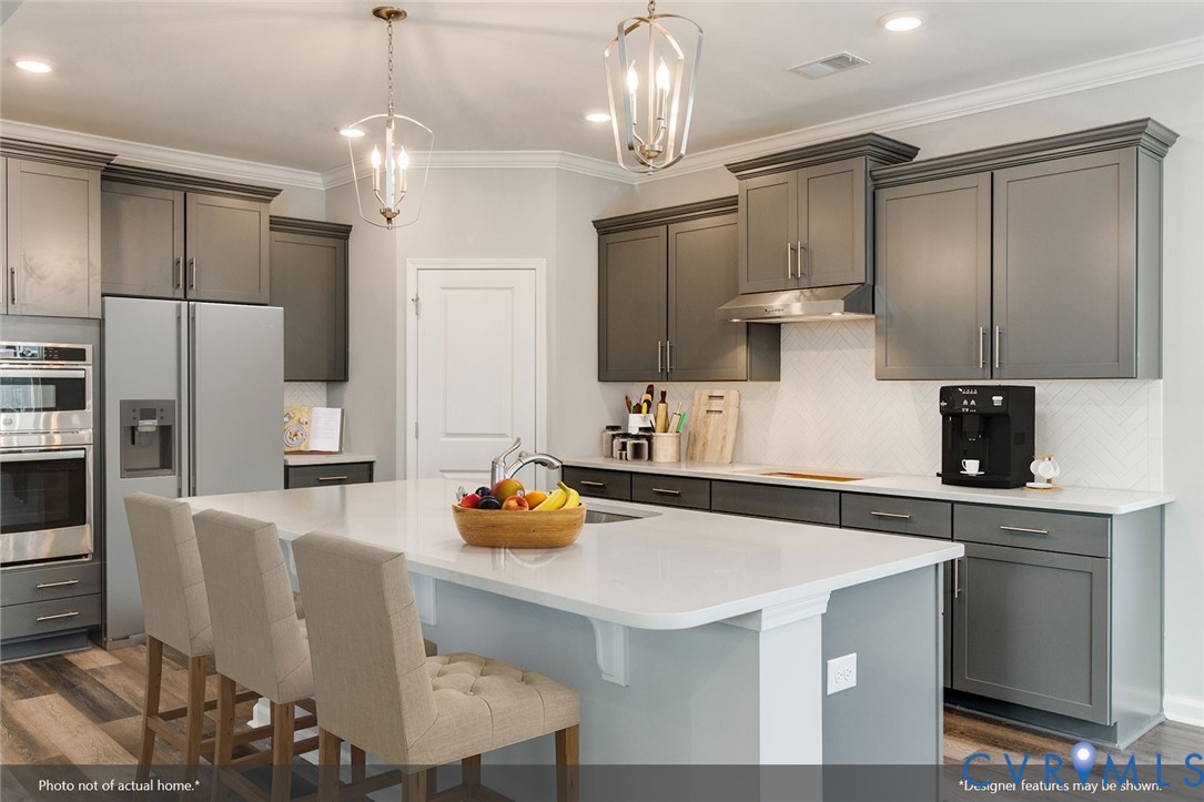 Modern kitchen with gray cabinetry, a white island, stainless appliances, and pendant lights.