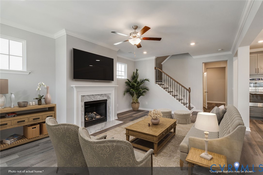 Staged living room with a marble fireplace, wall-mounted TV, staircase, and gray seating.