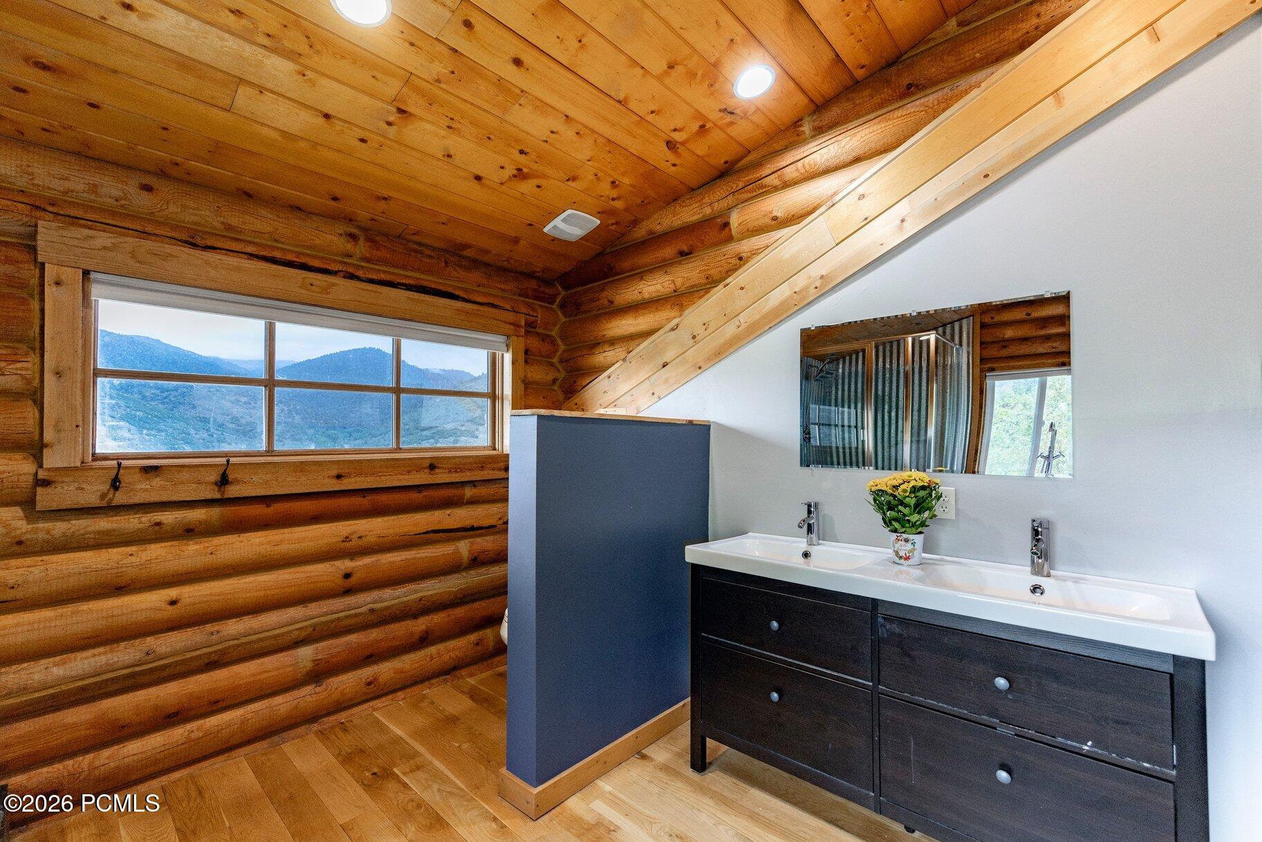 Rustic log-cabin bathroom with a double vanity and mountain views through the window.