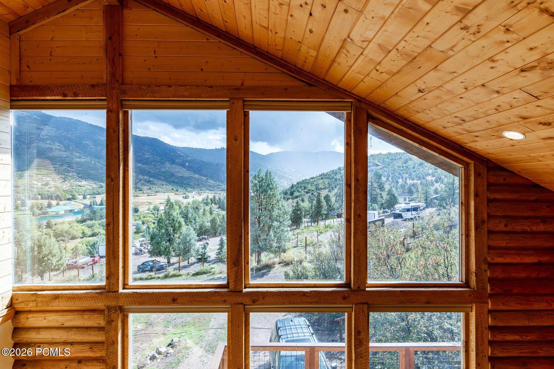 Vaulted wood interior with expansive windows overlooking a green mountain valley.