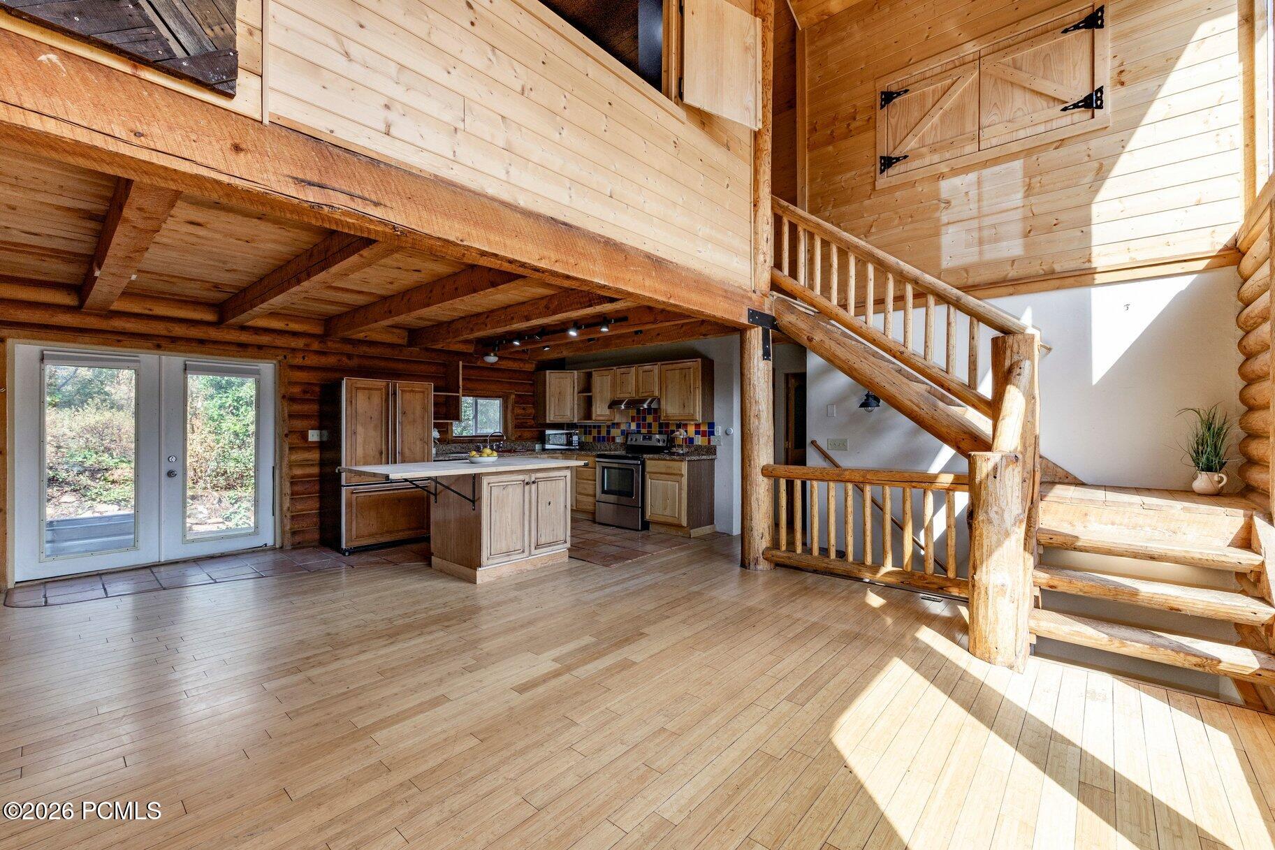 Open cabin kitchen and living area with exposed beams and a rustic staircase to the loft.