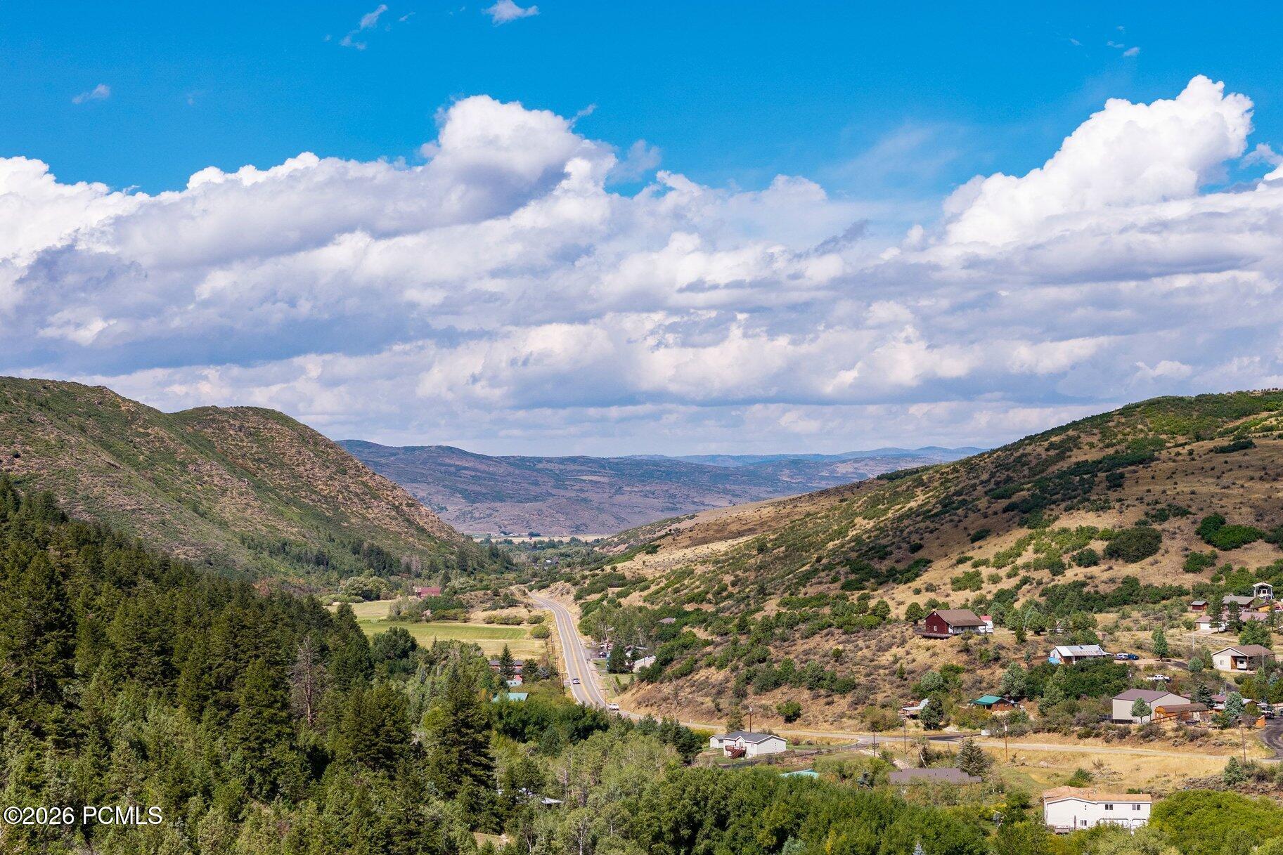 Rural mountain valley with a winding road, scattered homes, and cloud-filled blue sky