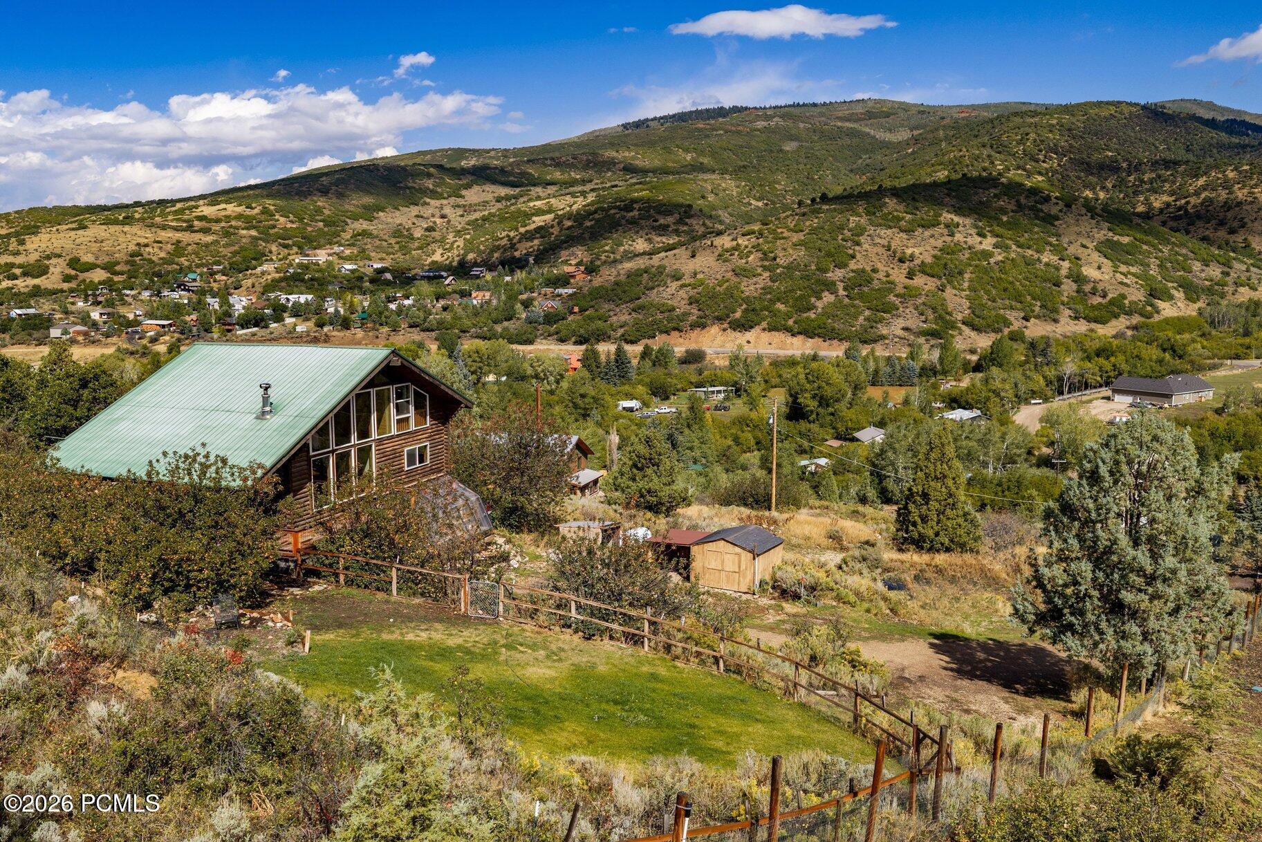 Log cabin with a green metal roof overlooking a fenced yard and mountain valley.