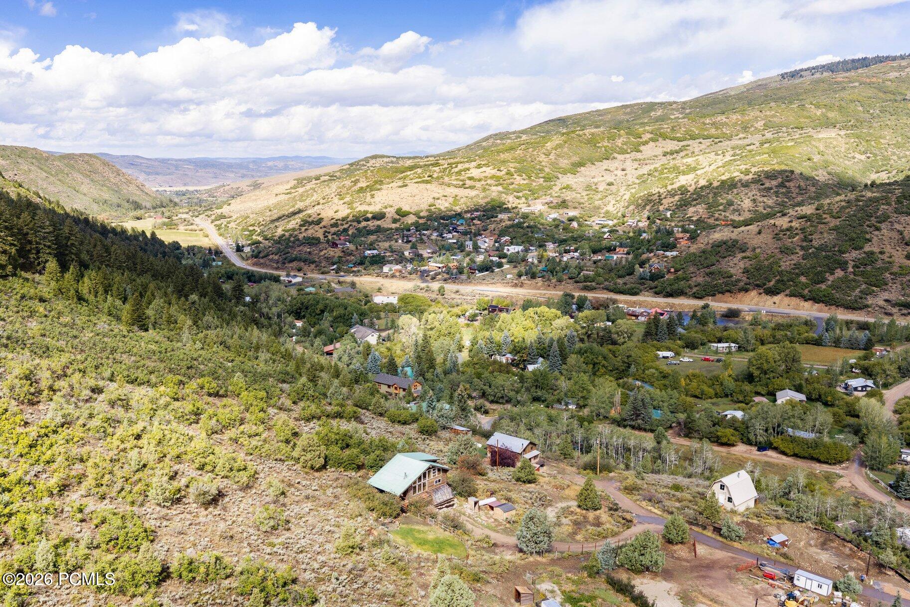Aerial view of a mountain valley neighborhood with scattered homes, wooded slopes, and a winding road.