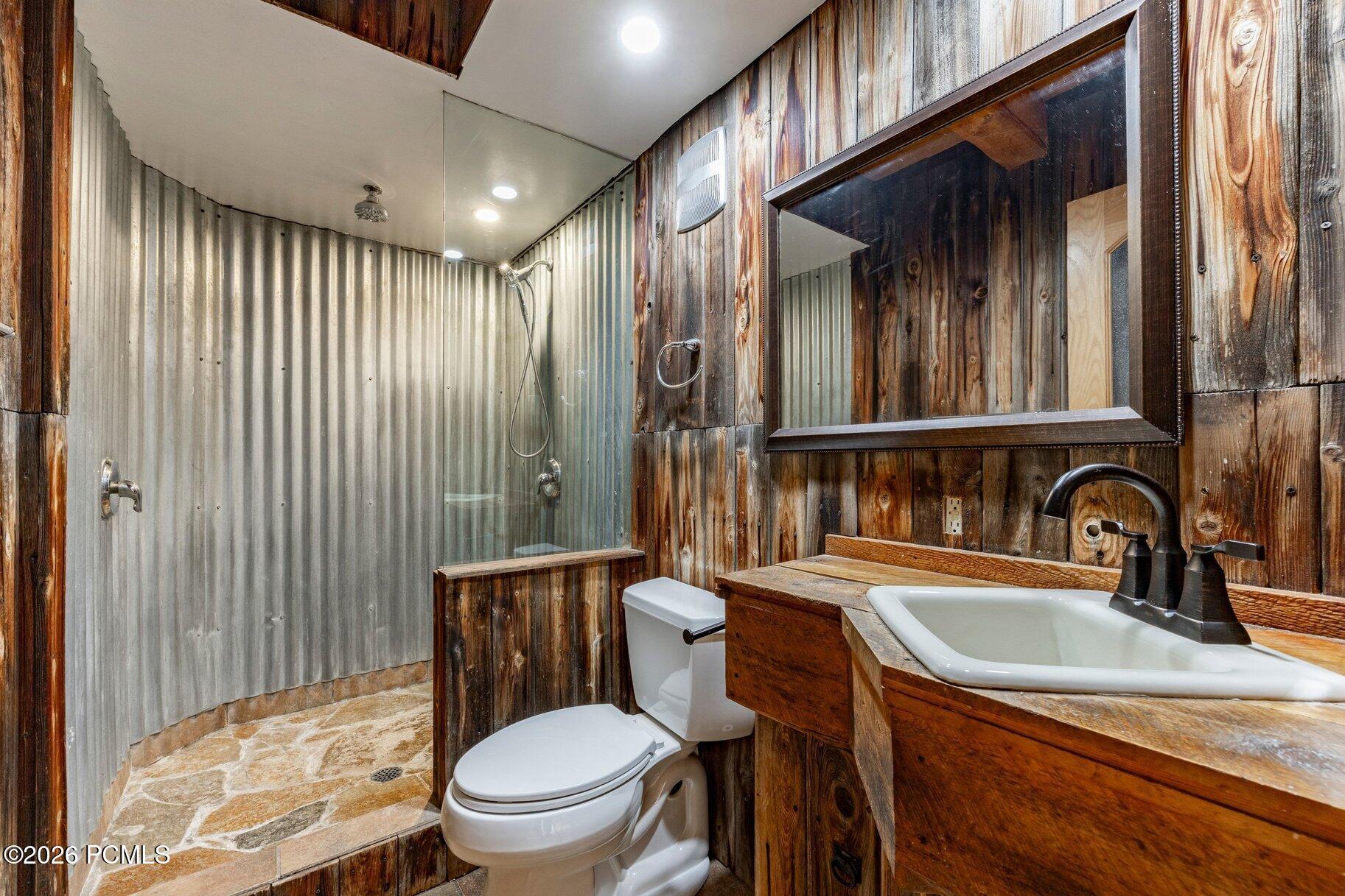 Rustic bathroom with a corrugated metal shower and a wooden vanity with a white sink.