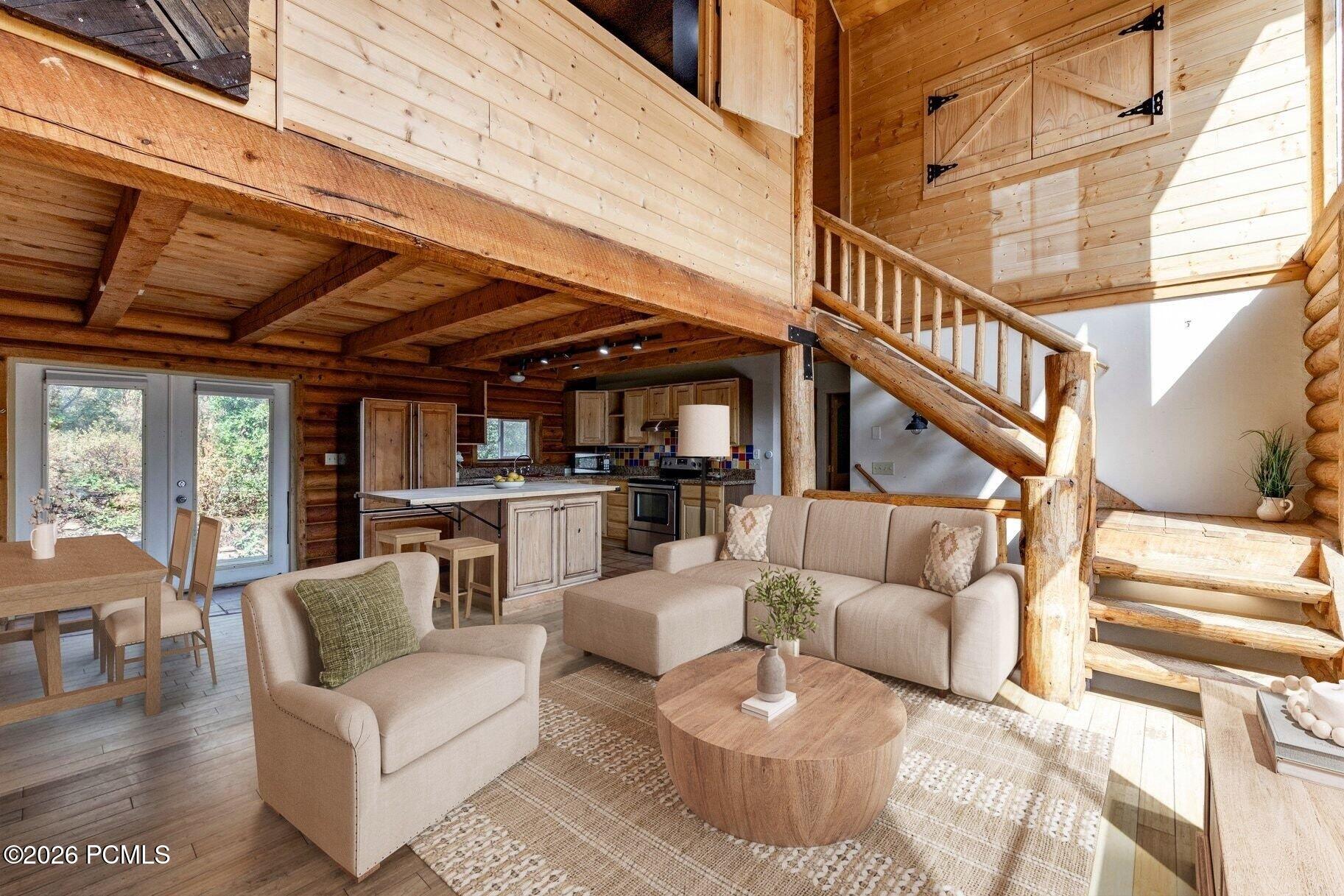 Open-plan cabin living room and kitchen beneath a timber loft, with a rustic staircase and exposed beams.