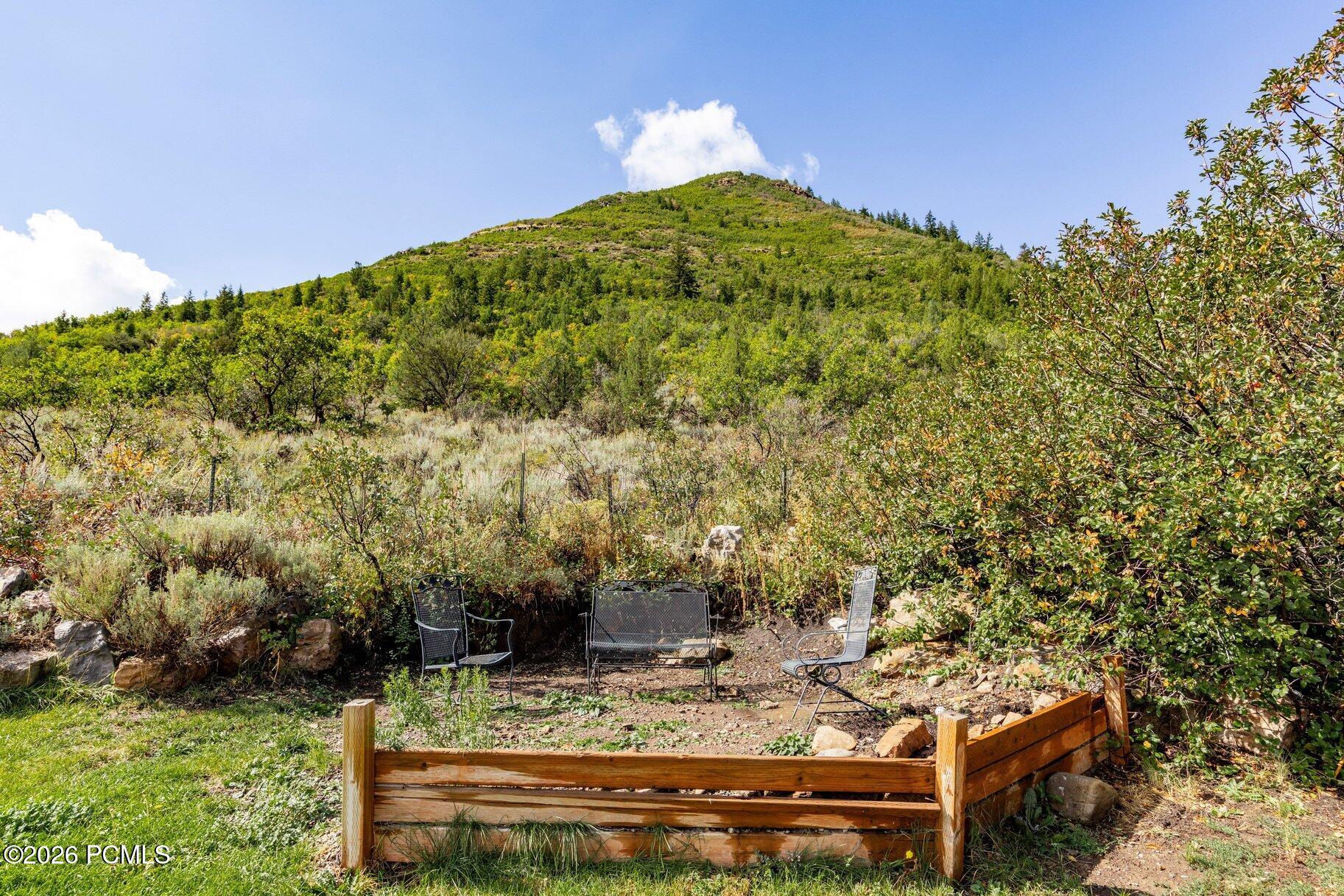Outdoor seating area facing a green hillside, with metal chairs and a low wooden border.