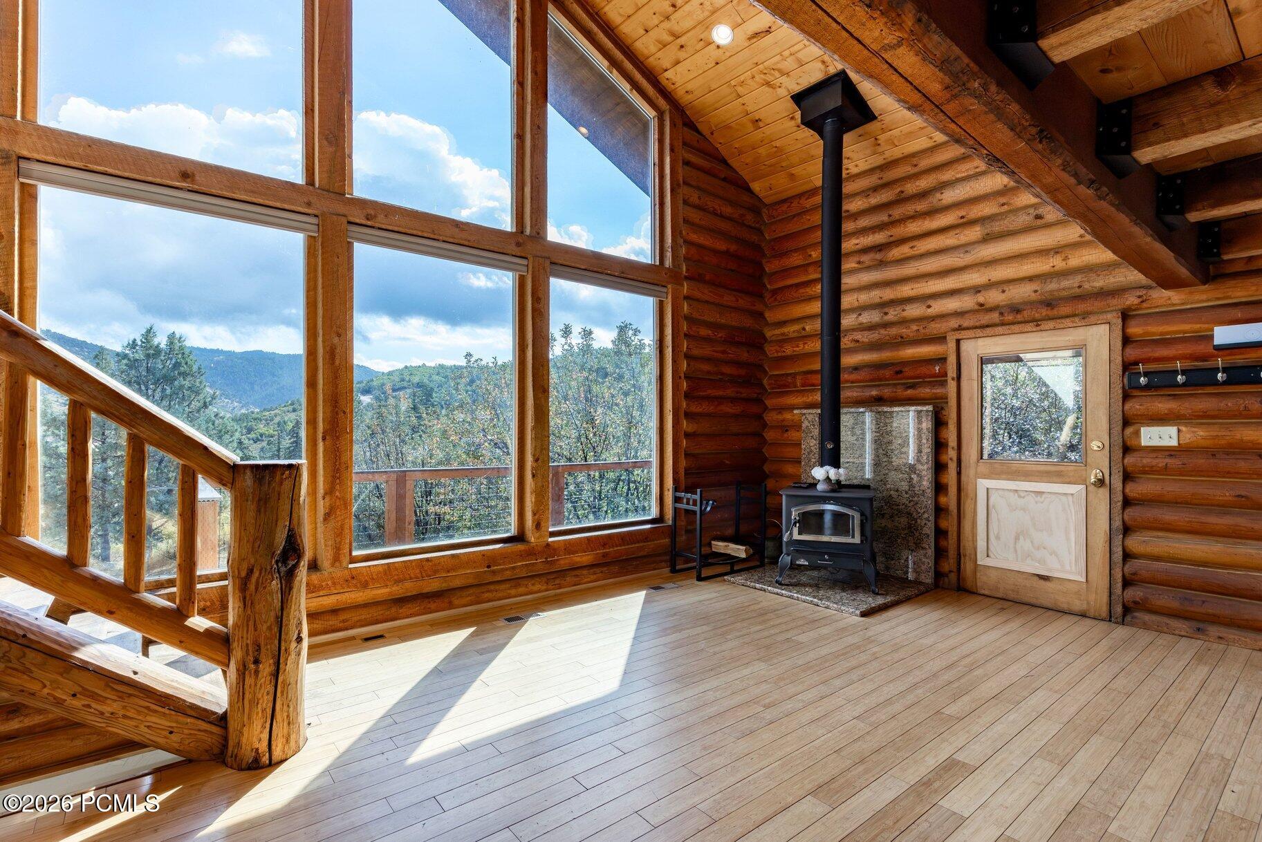 Log cabin interior with a wood stove and large windows overlooking forested mountains.