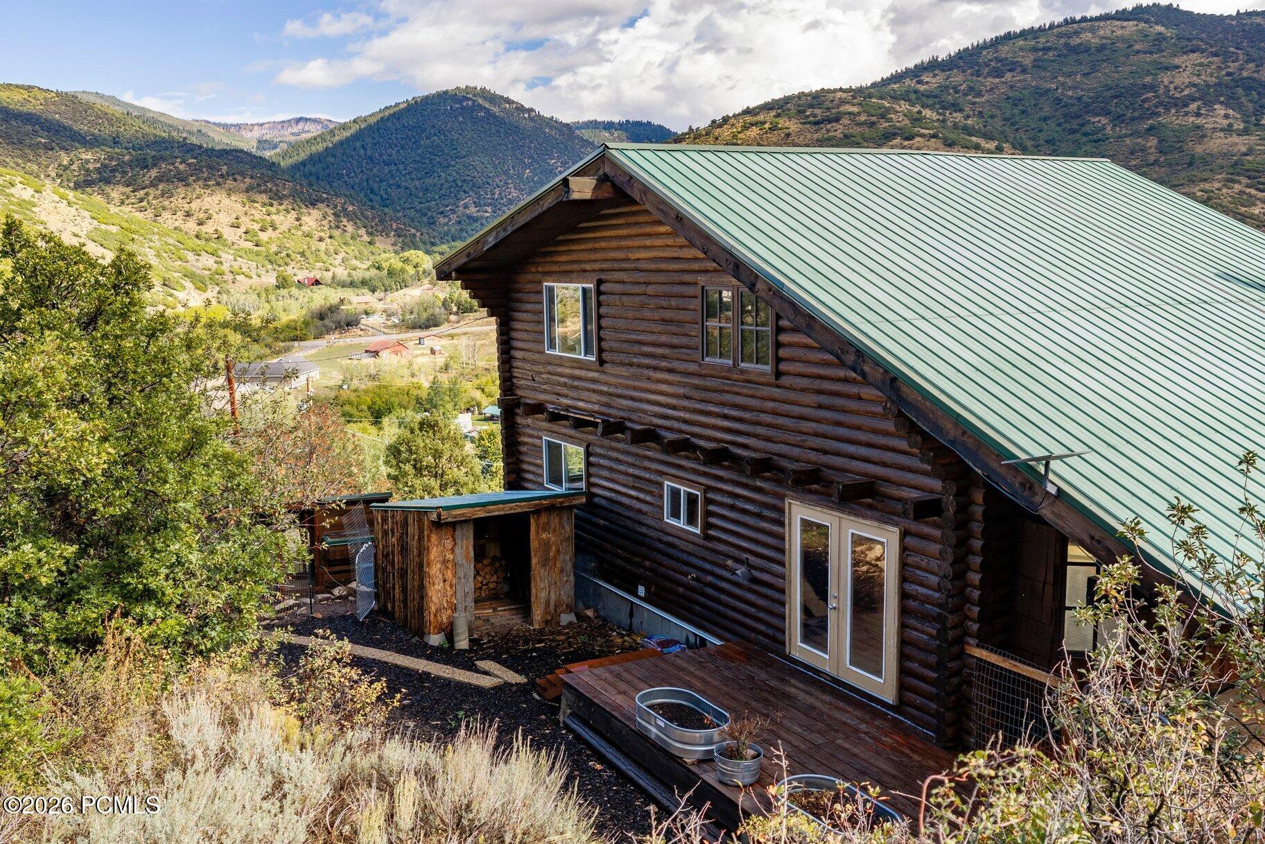 Log cabin with a green metal roof and deck overlooking a mountain valley.