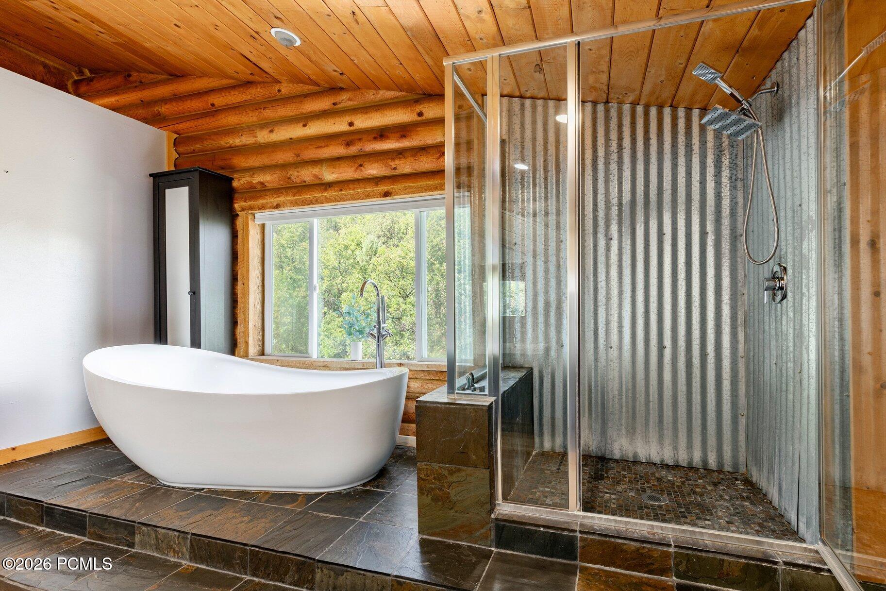 Bathroom with a freestanding soaking tub, glass shower, corrugated metal walls, and timber ceiling.