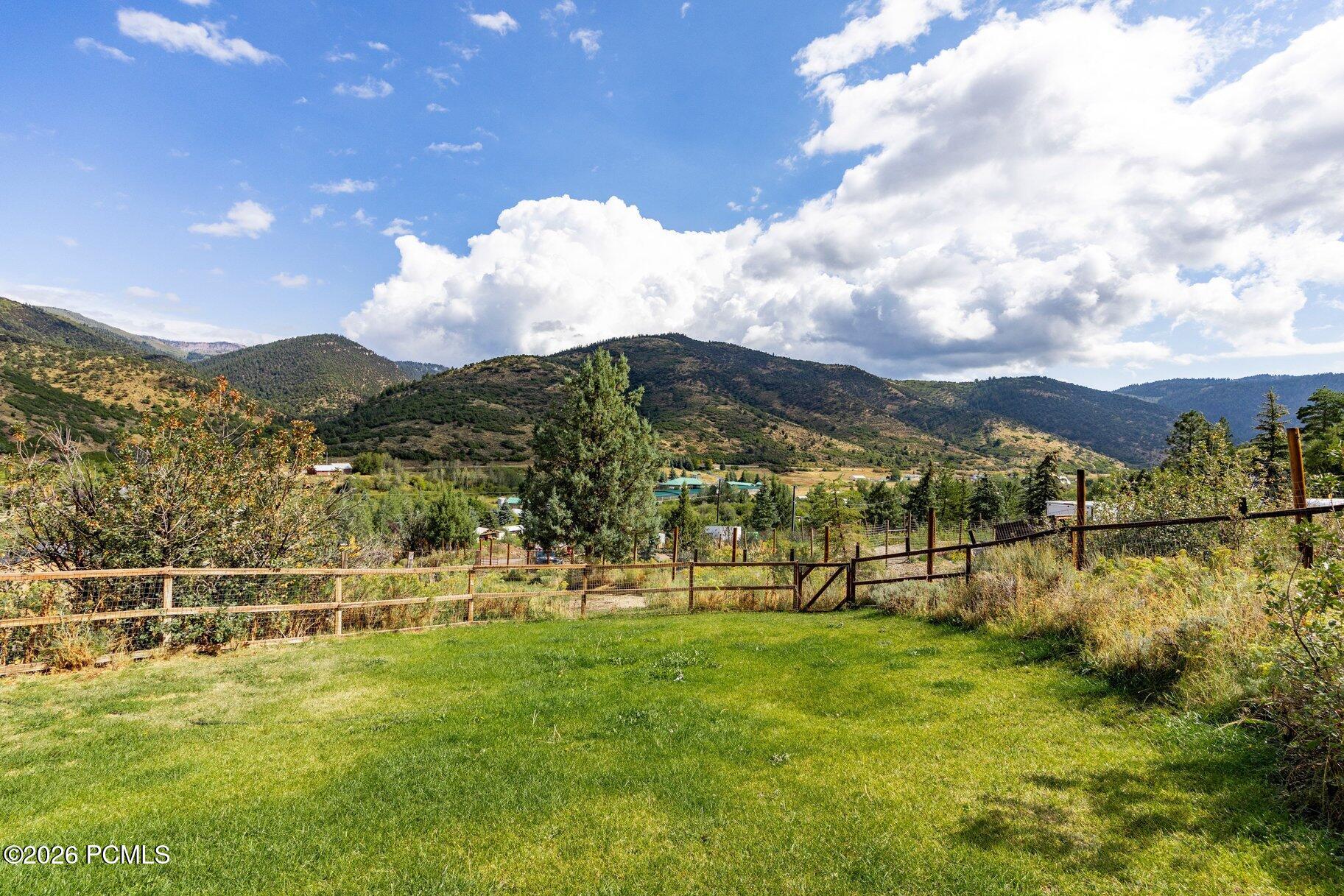 Fenced grassy yard with a wide view of forested mountains and valley.
