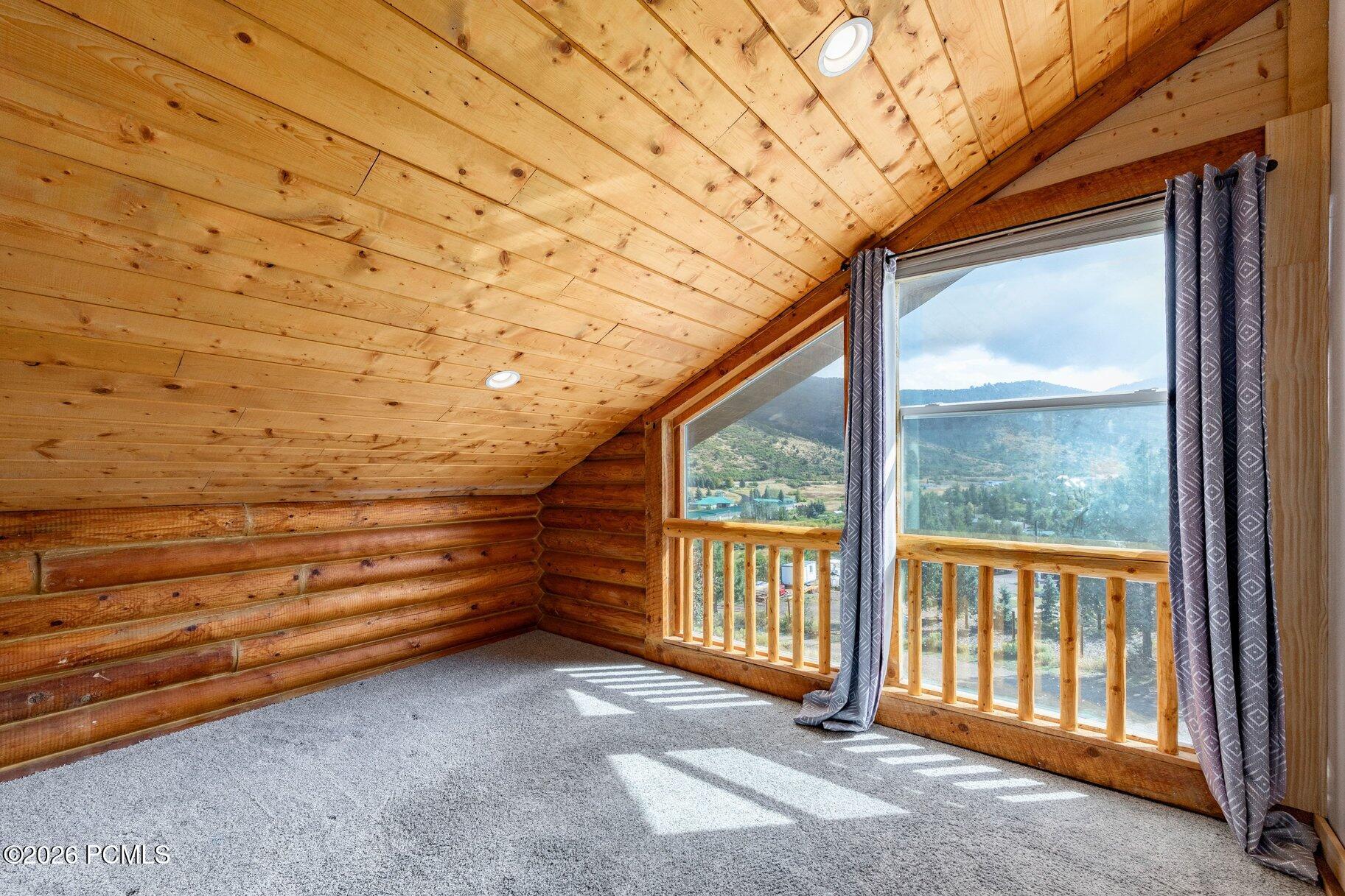 Unfurnished log room with a sloped wood ceiling and large windows overlooking a mountain valley.
