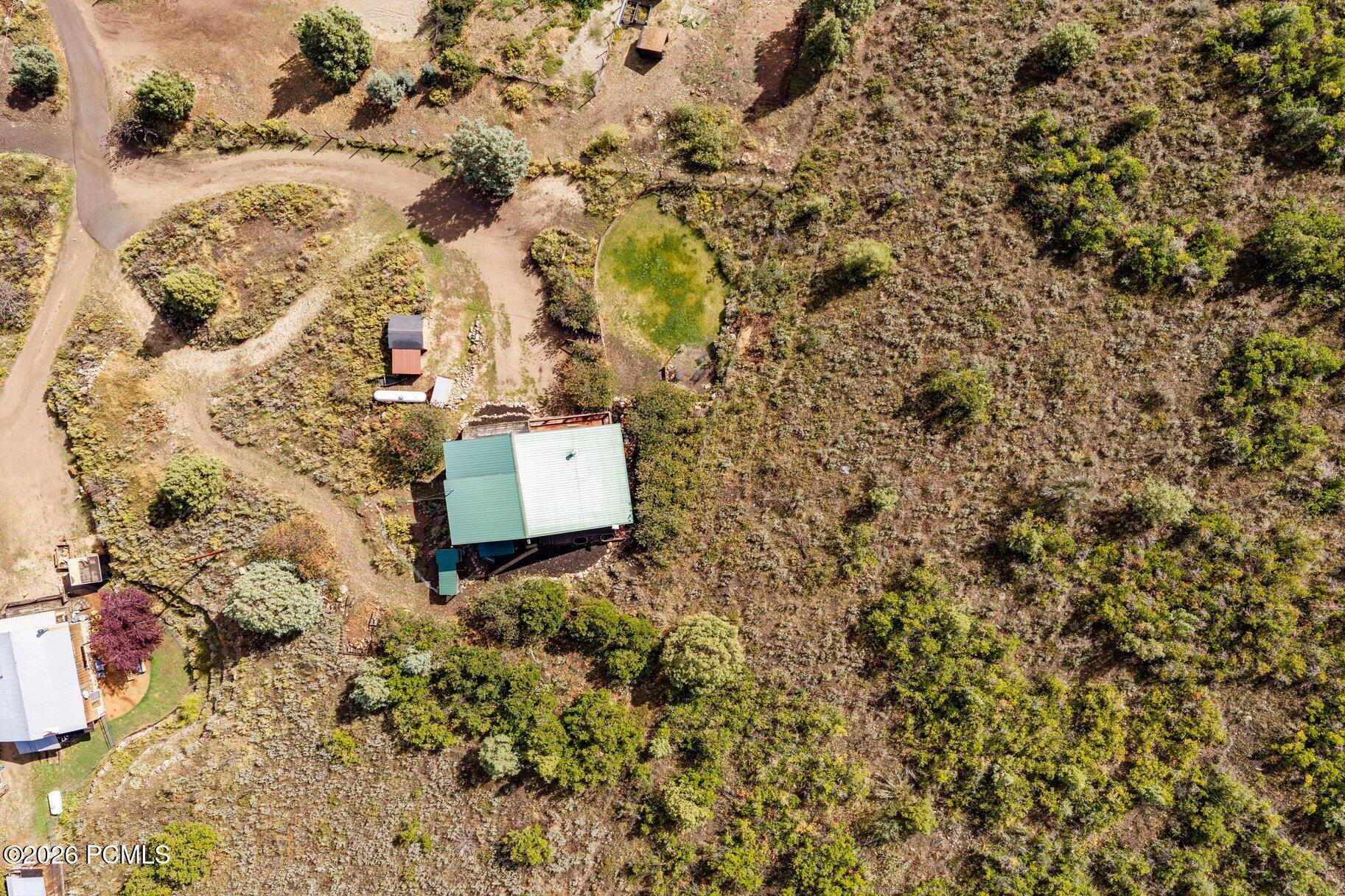 Aerial view of a green-roofed house amid scrubland, with a curving driveway and circular lawn.