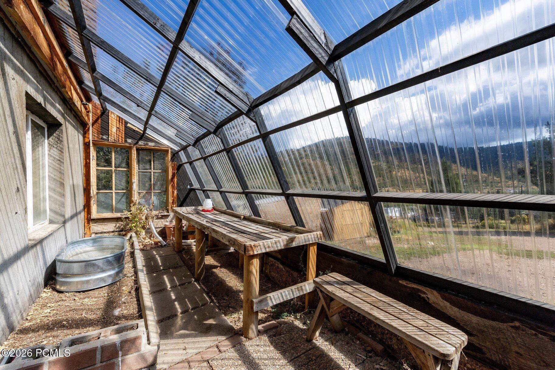 Attached greenhouse with wooden benches, planting beds, and a translucent roof overlooking the countryside.