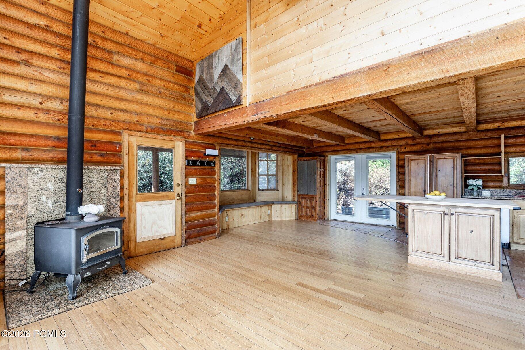 Log-cabin kitchen and living area with exposed beams, a wood stove, and a light-wood island.