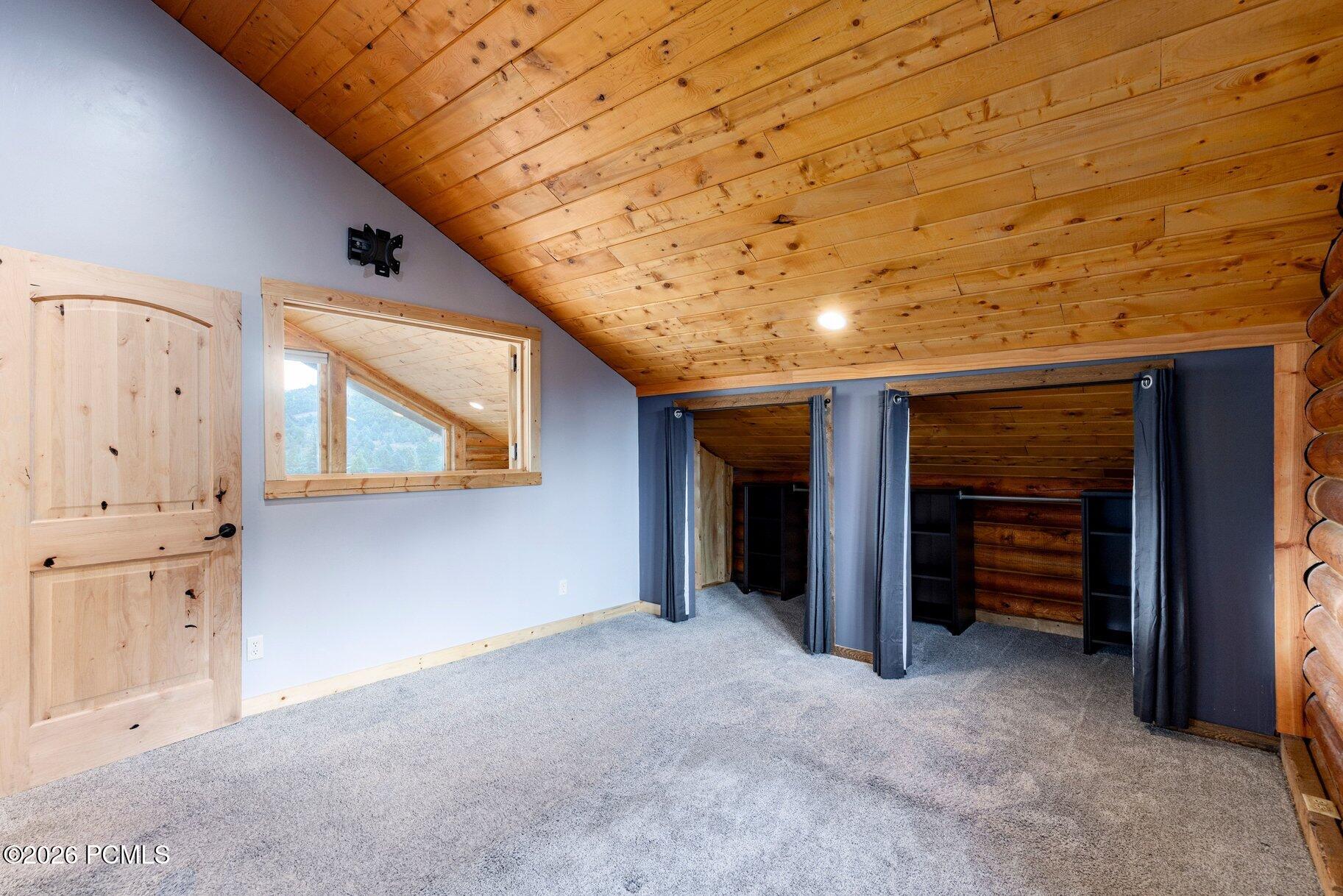 Unfurnished bedroom with a sloped knotty-pine ceiling and curtained closet alcove.