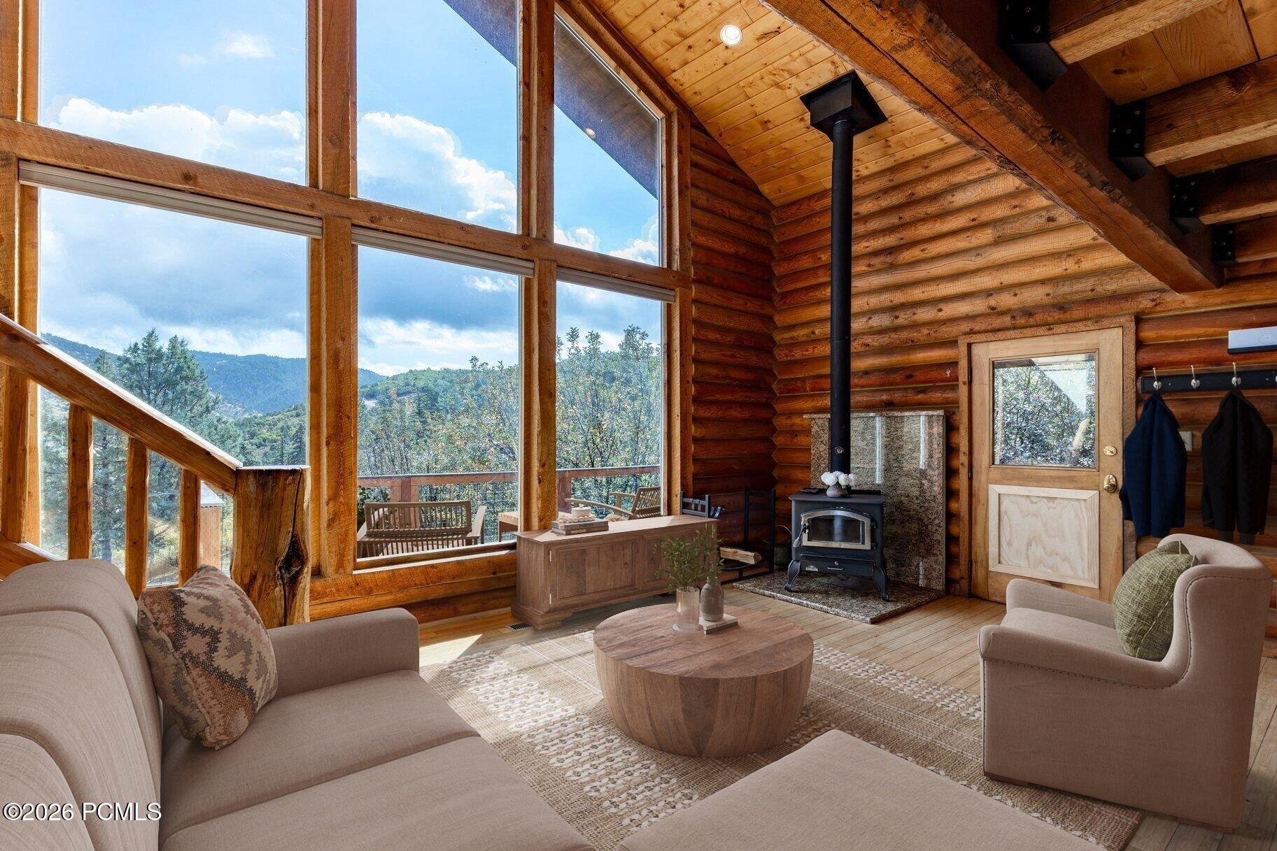 Log-cabin living room with vaulted timber ceiling, mountain-view windows, and a freestanding wood stove.