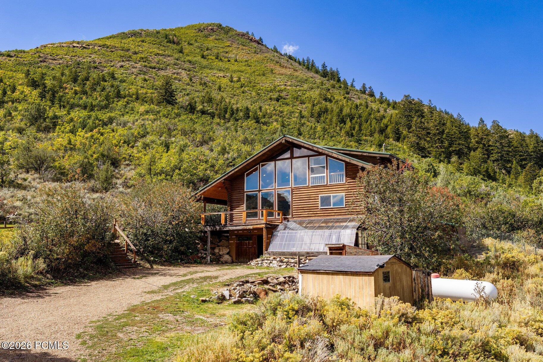 Log-sided mountain home with a tall wall of windows, deck, and gravel drive.