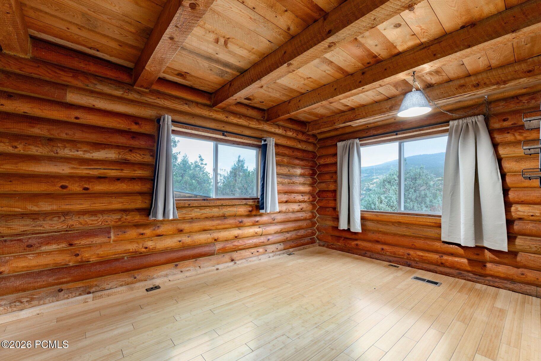 Empty log-cabin interior with exposed timber beams and curtained windows overlooking a mountain.