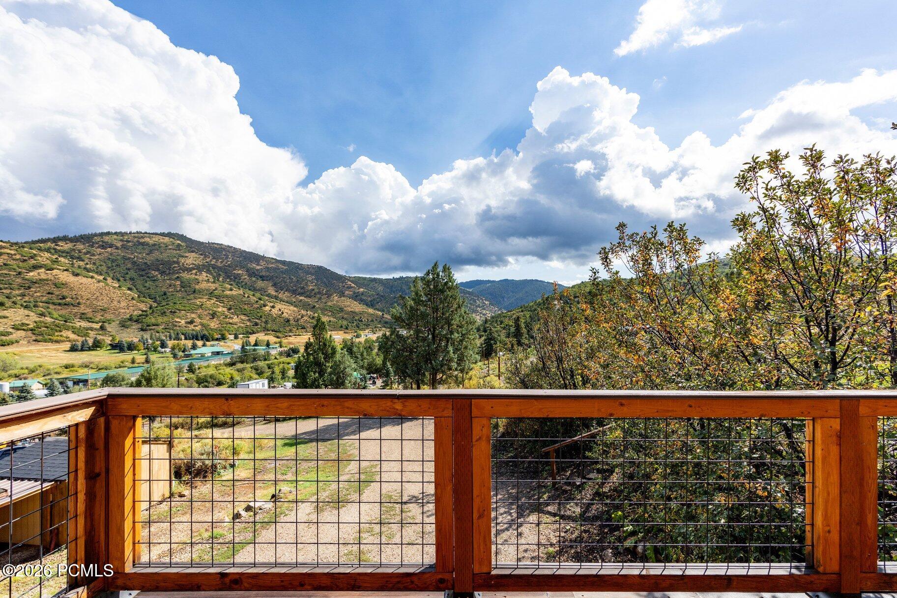 Mountain valley seen from a wooden deck with a wire-grid railing and autumn-colored trees.