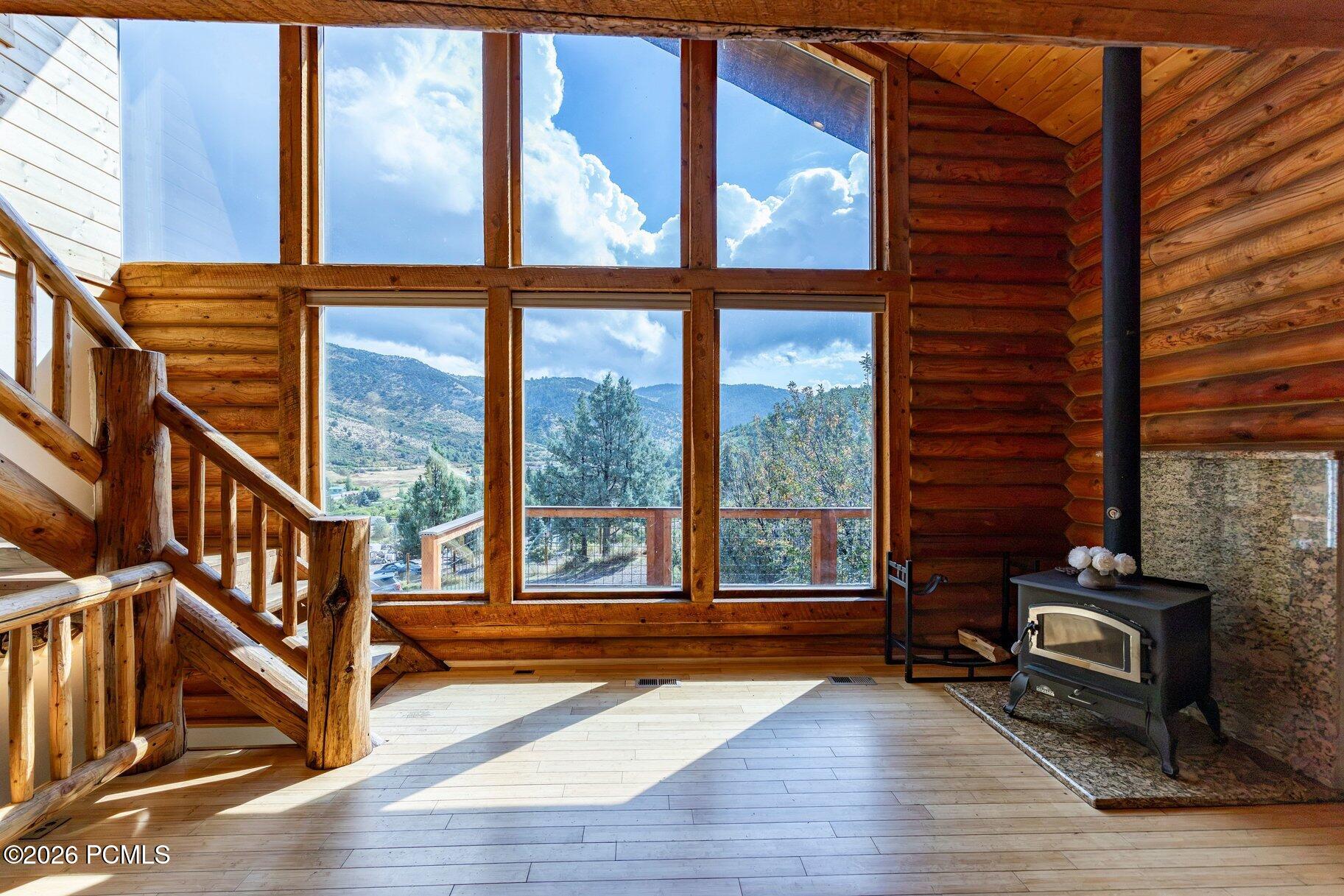 Log-cabin living room with soaring windows, mountain views, a rustic staircase, and a wood-burning stove.