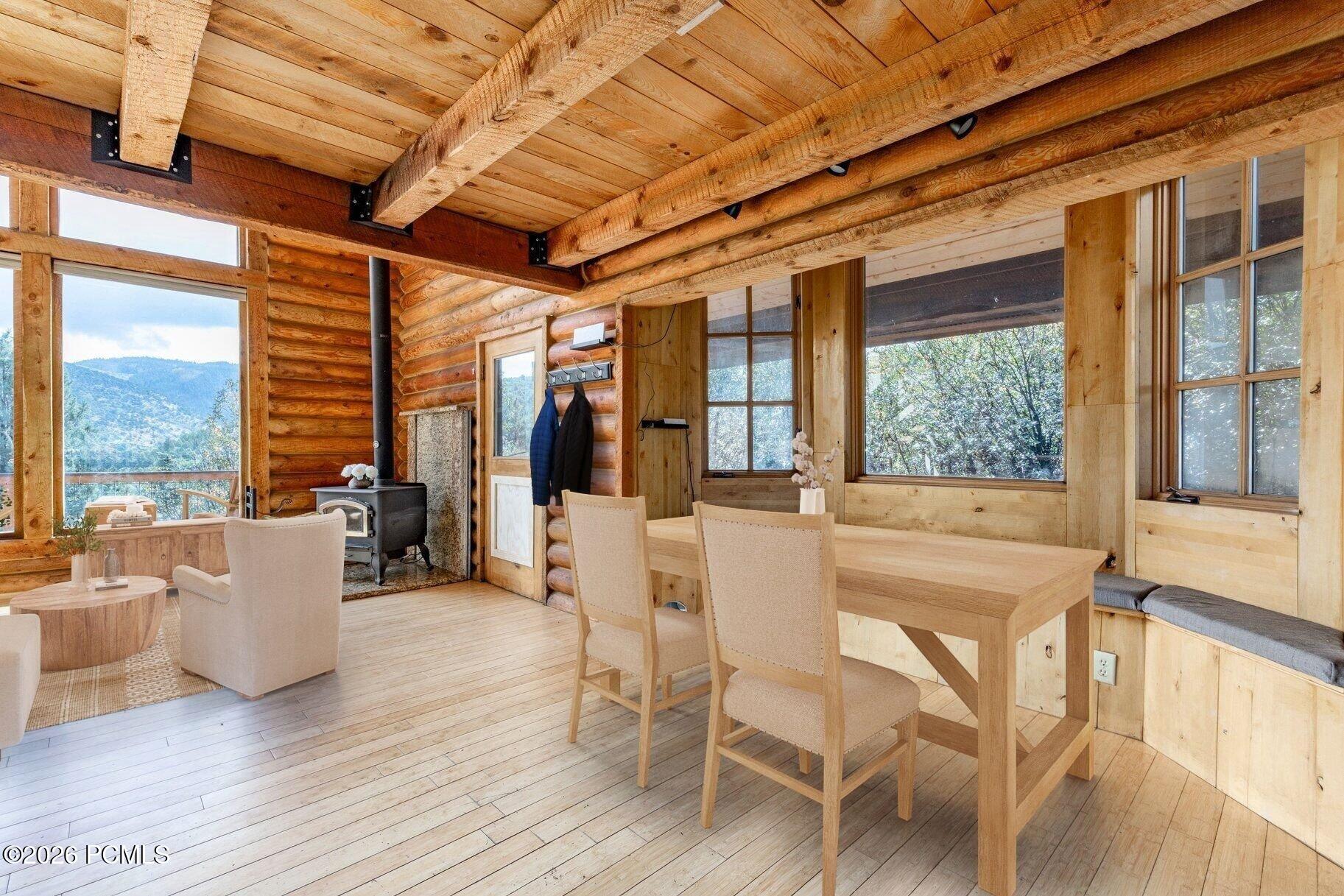 Log-cabin dining and living area with exposed beams, a wood stove, and mountain views through large windows.
