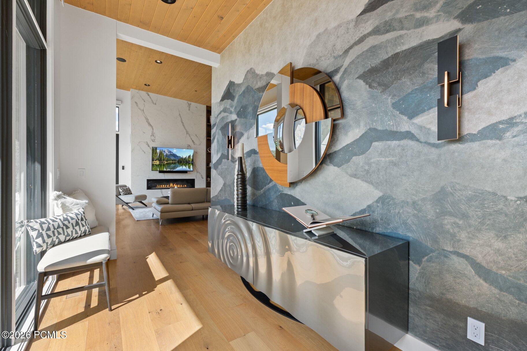 Modern living room with a mountain-pattern wall, sculptural mirror, wood ceiling, and fireplace.