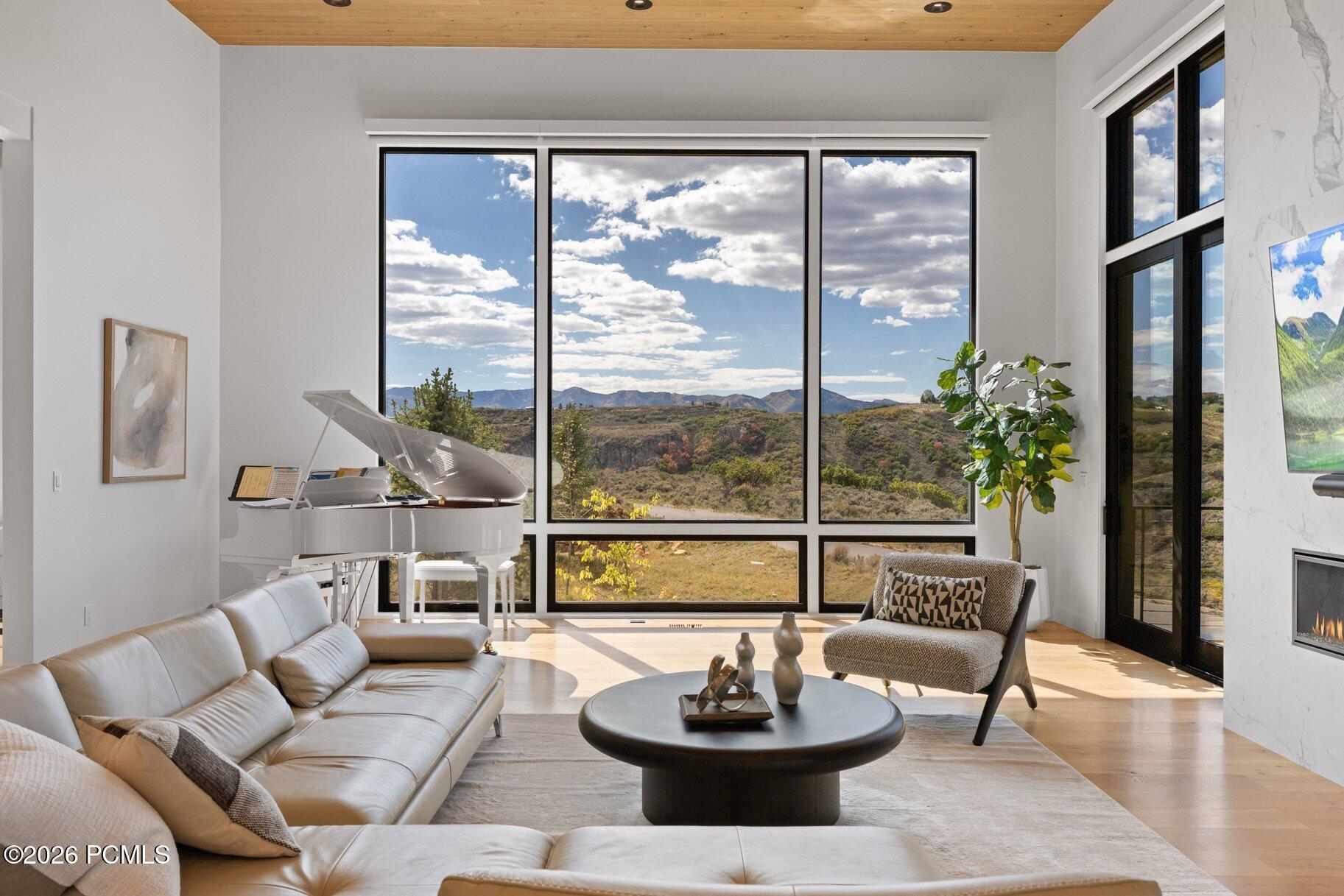 Living room with a white grand piano and expansive windows overlooking autumn hills and mountains.
