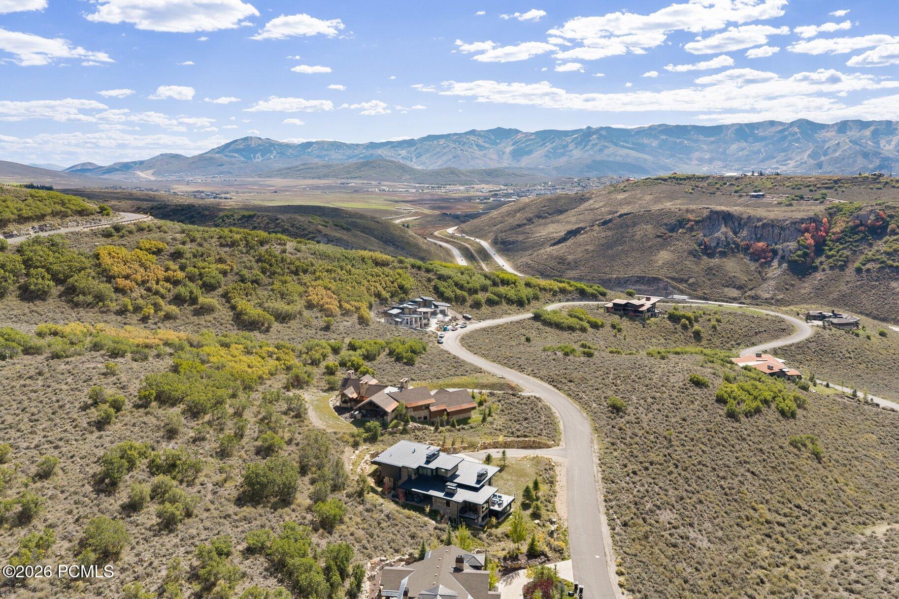 Aerial view of hillside homes along a winding road, with a broad mountain valley beyond.