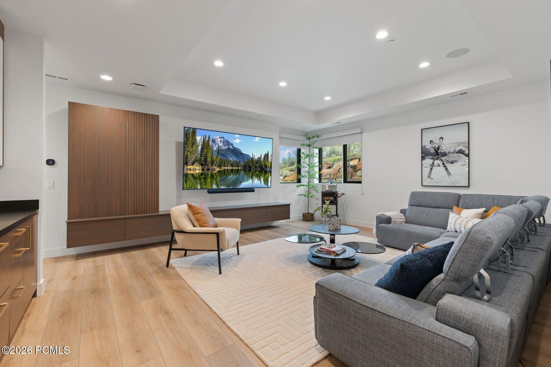 Modern living room with gray sectional, cream chair, wood cabinetry, and a wall-mounted television.