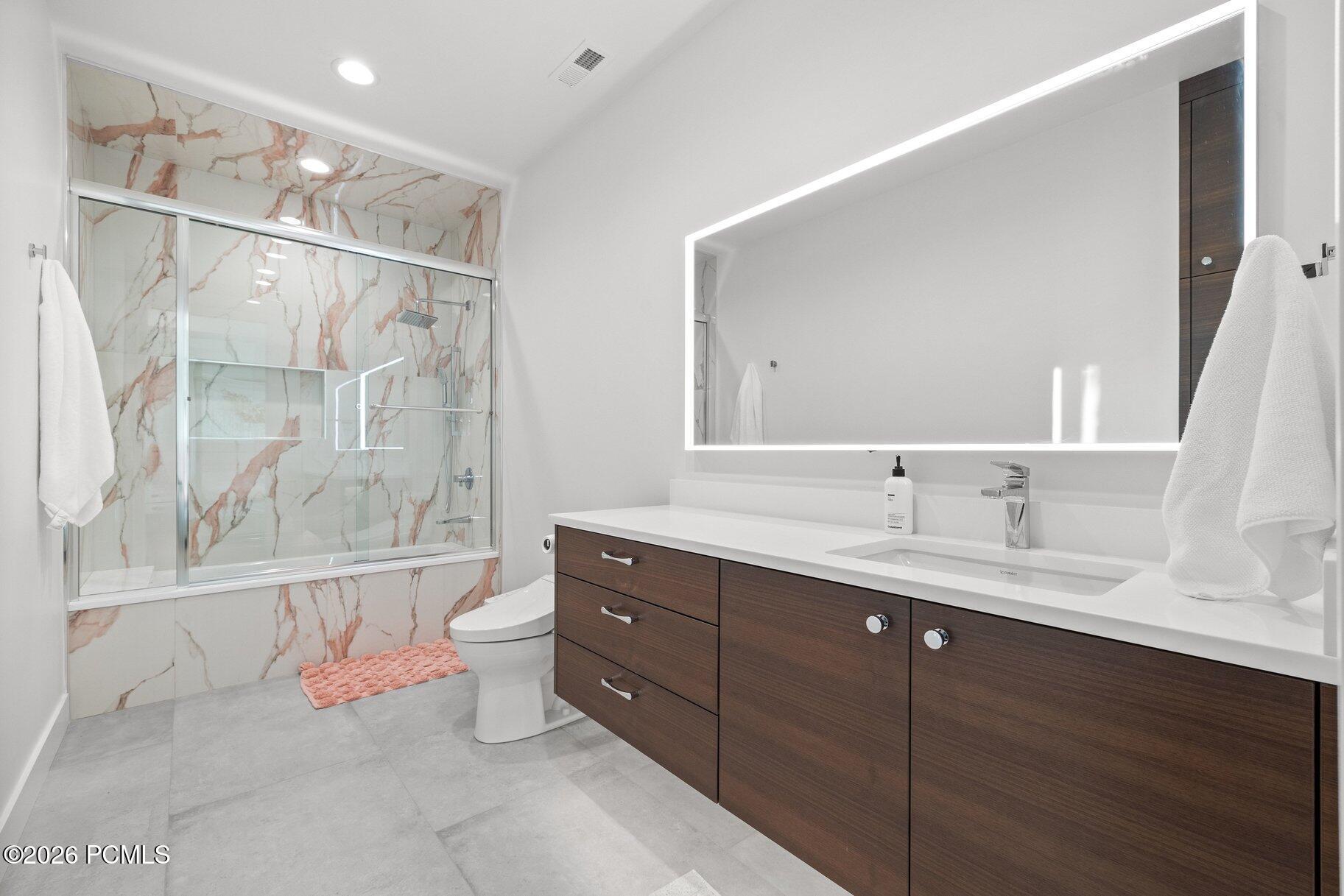 Modern bathroom with a veined marble shower, dark wood vanity, and illuminated mirror.