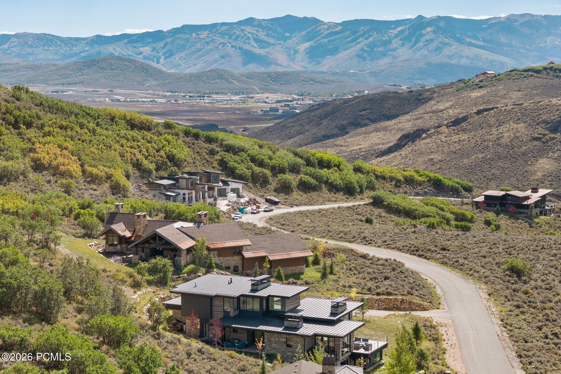 Aerial view of a modern hillside home with a winding road and mountain ranges in the distance.