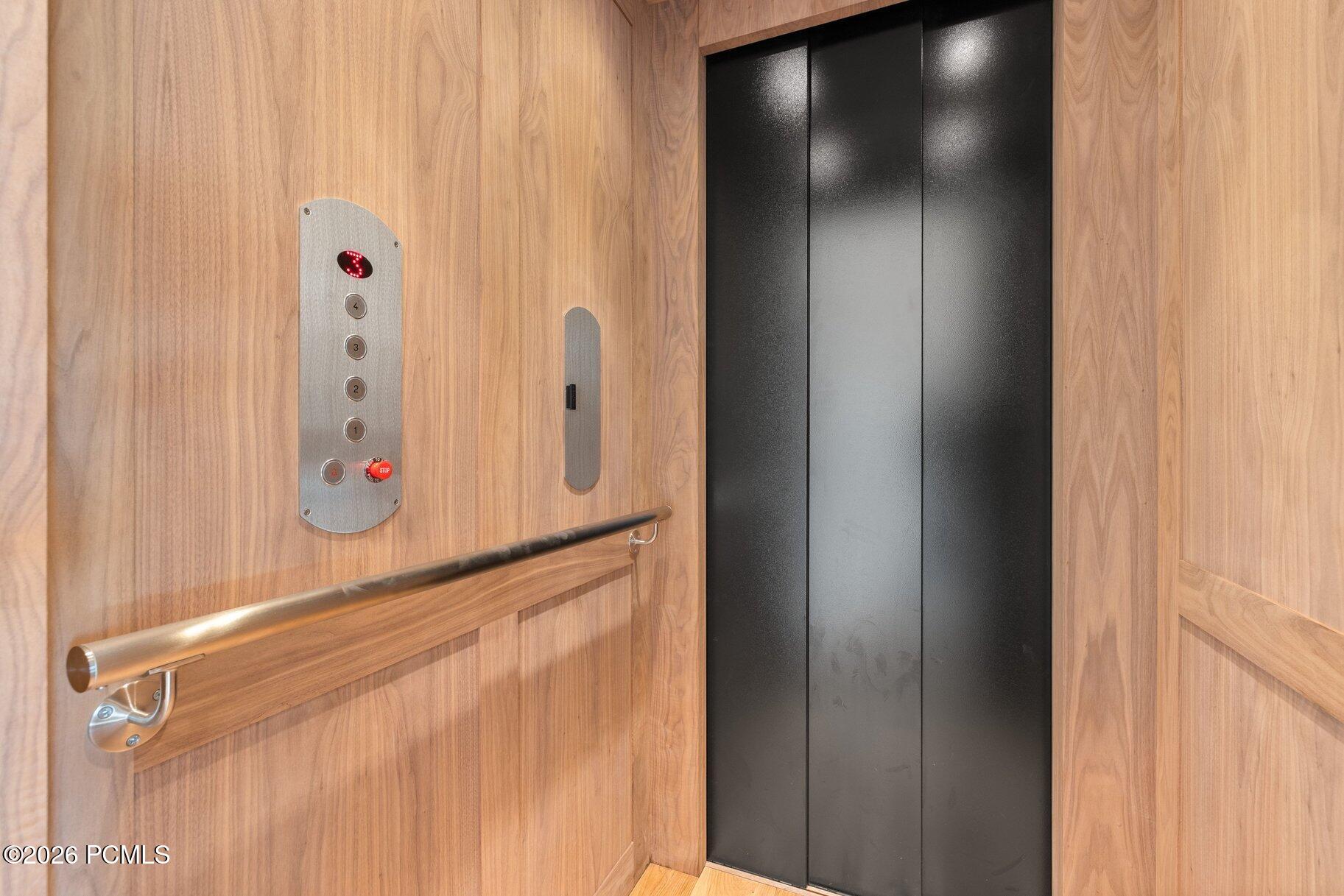 Wood-paneled elevator with a metal handrail and dark doors.