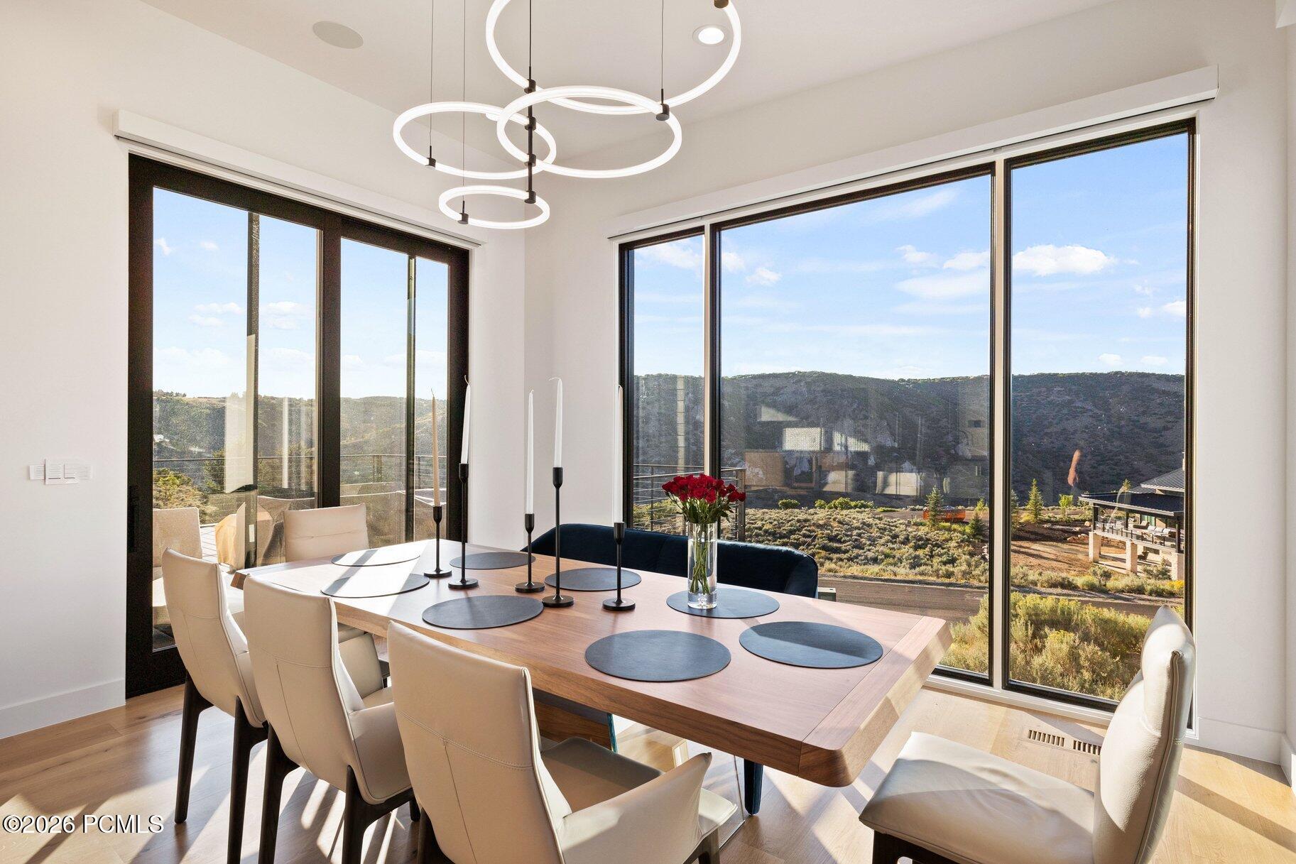 Modern dining room with ring pendant lights and wide windows overlooking wooded hills.