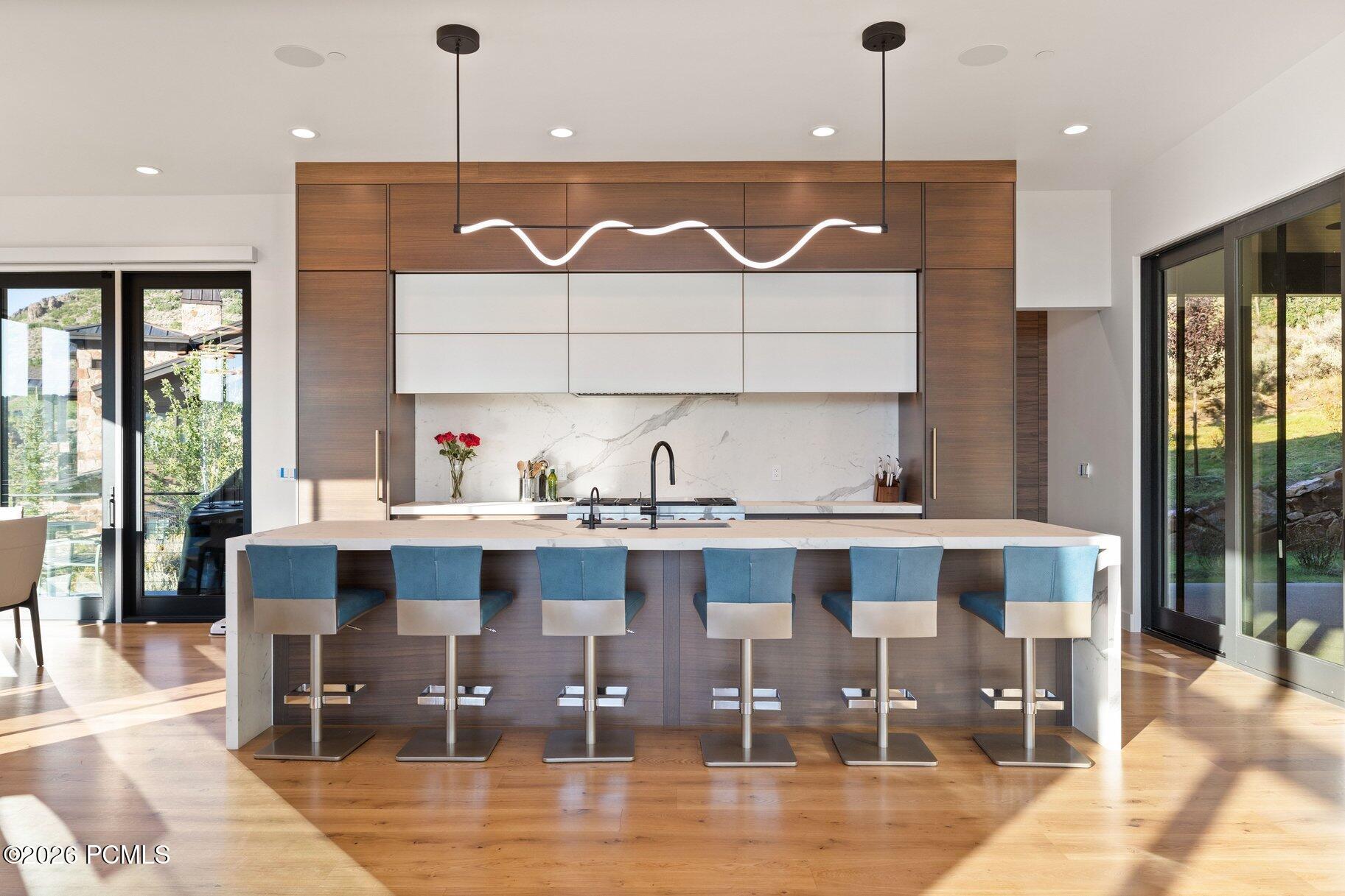 Modern kitchen with a marble island, six blue stools, walnut cabinetry, and a sculptural pendant light.