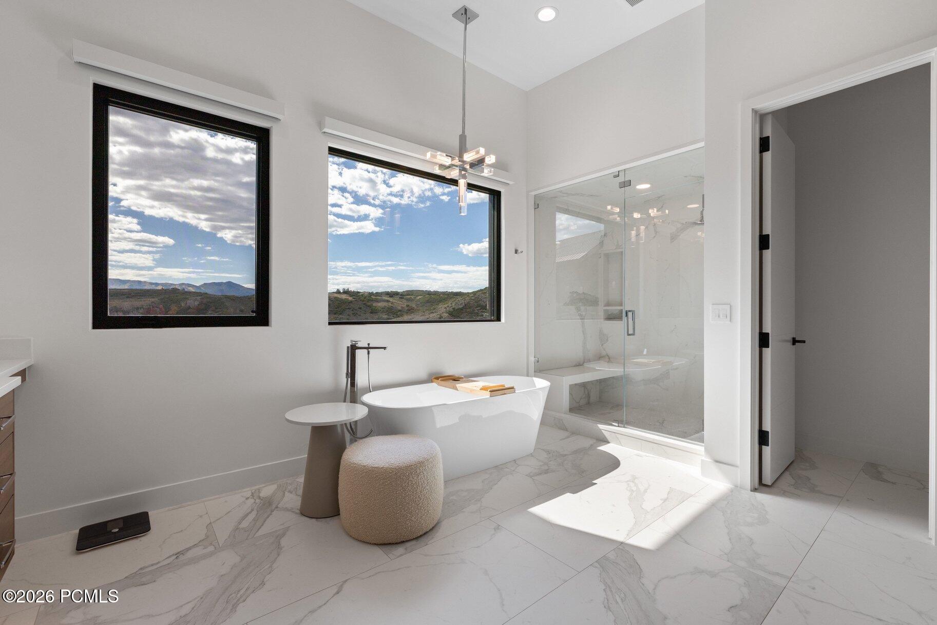 Modern bathroom with a freestanding tub, glass shower, and mountain views through large windows.