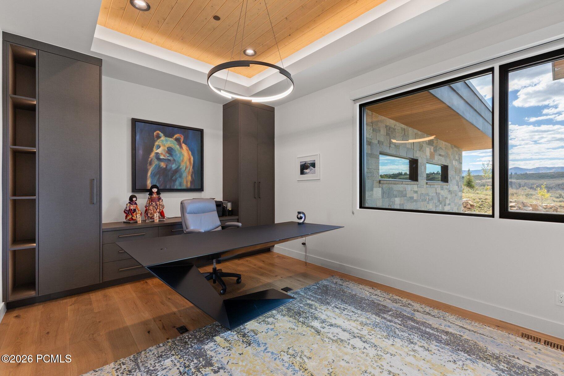 Modern home office with built-in cabinetry, a sculptural desk, and windows overlooking distant hills.