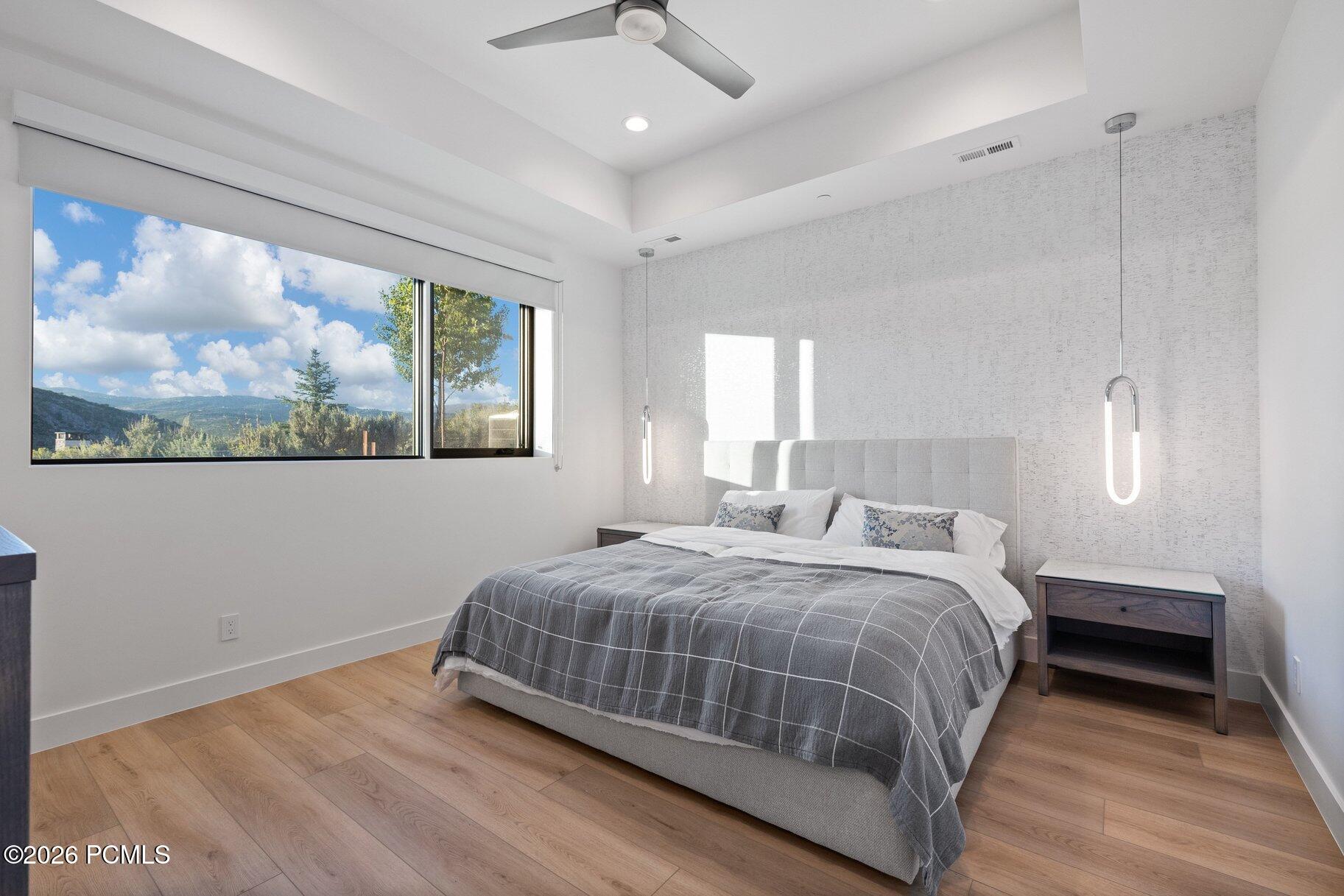 Modern bedroom with a gray plaid bed and a large window overlooking wooded mountain scenery.