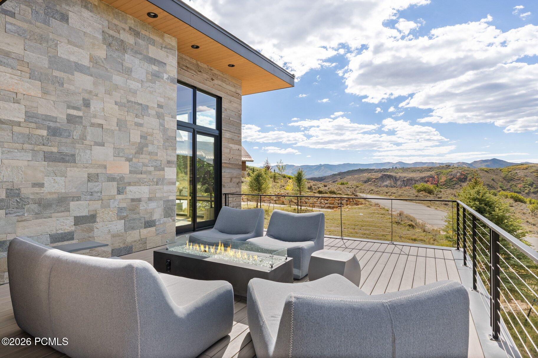 Modern home deck with lounge seating and fire table overlooking mountain ridges.