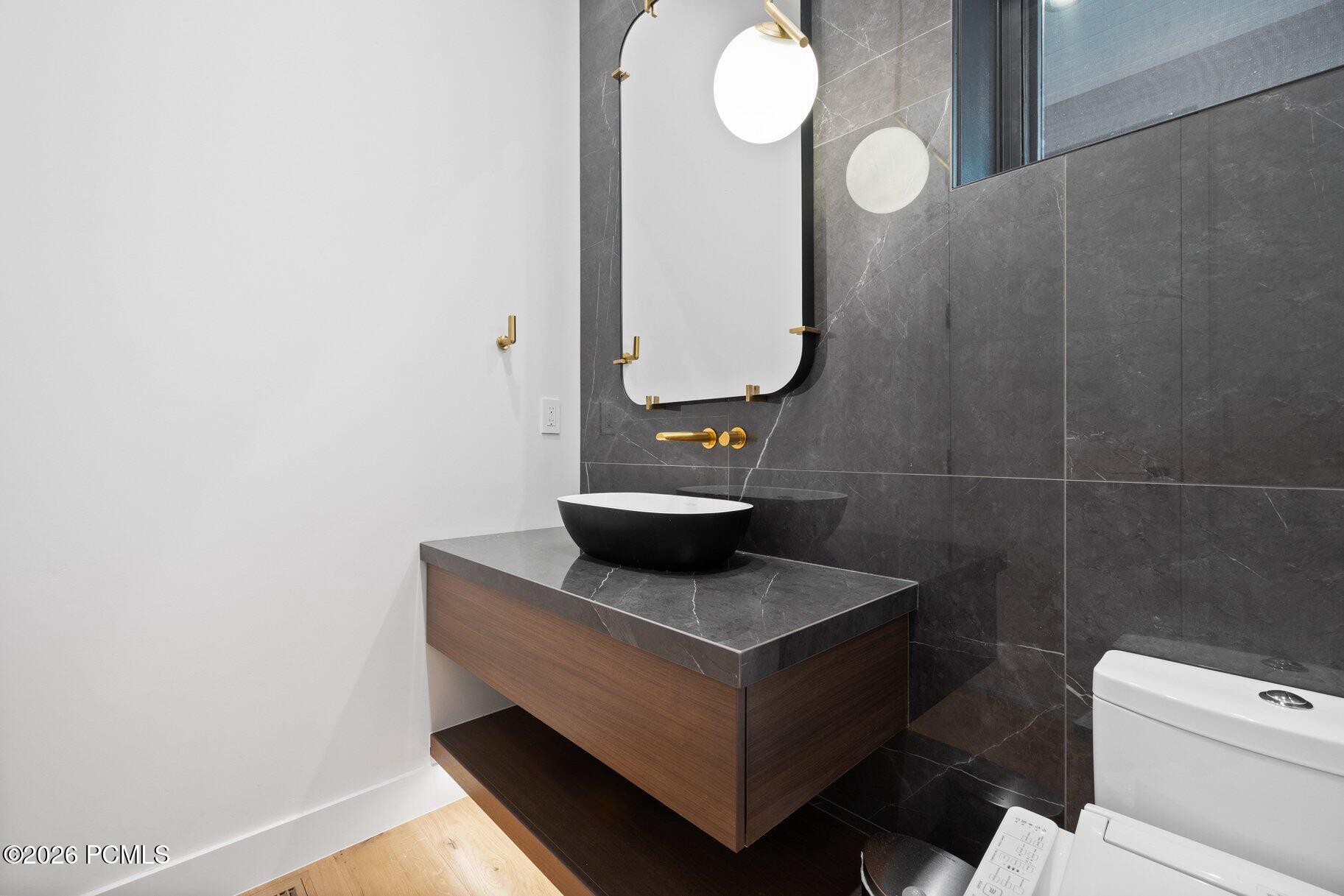 Modern bathroom vanity with a black vessel sink, floating wood cabinet, dark marble tile, and gold fixtures.