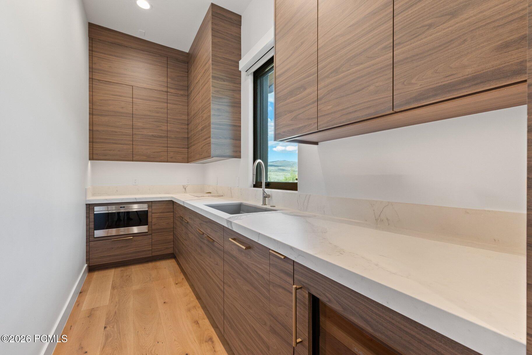 Modern kitchen with walnut cabinets, white stone counters, and a window overlooking green hills.